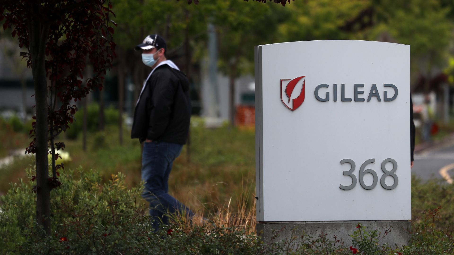 In this image, a masked man stands next to a sign for Gilead