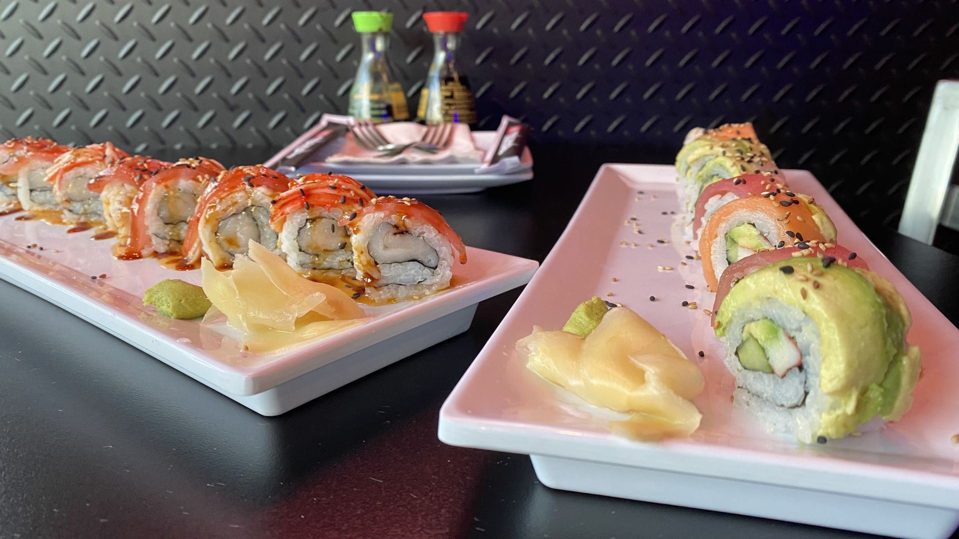 A photo of two long plates with sushi rolls divided into bites. 
