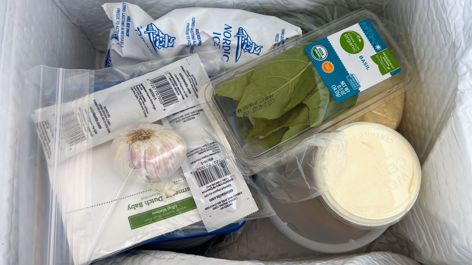 The inside of a meal kit full of supples such as basil, garlic , an ice pack and a container of cheese