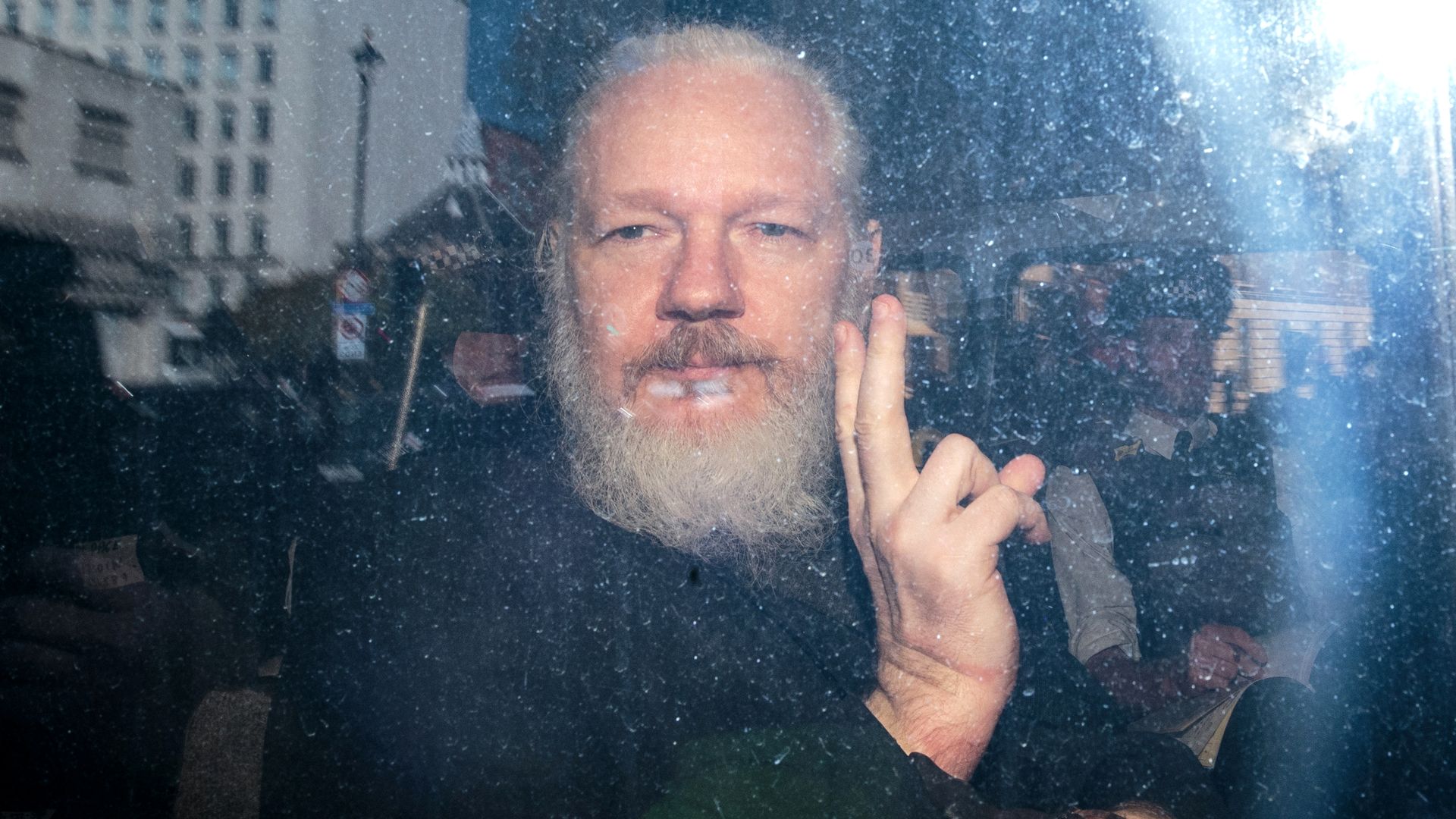 Assange makes a peace sign at the camera in this image.