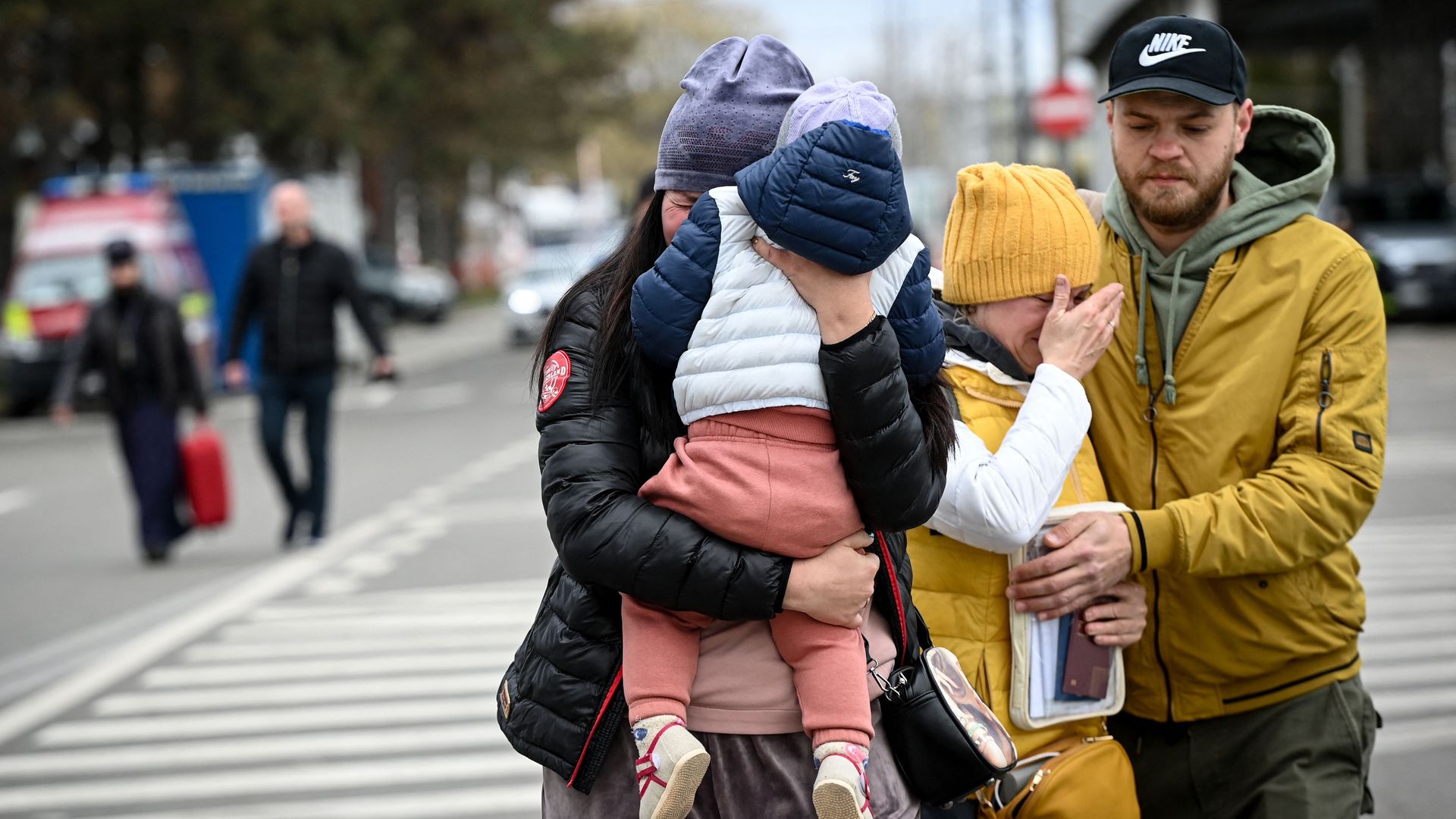 Picture of a woman holding a baby without looking at the camera, another woman covering her face and a man holding that second woman