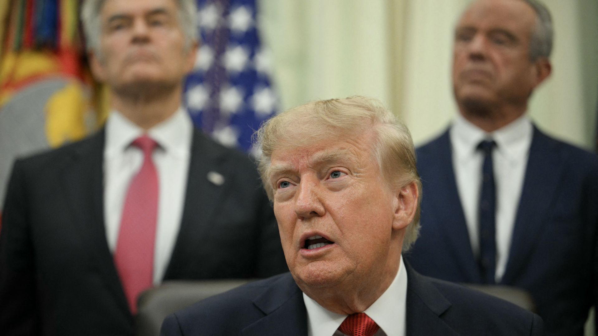 President Trump seated in the Oval Office, flanked by Mehmet Oz and Robert F. Kennedy Jr.