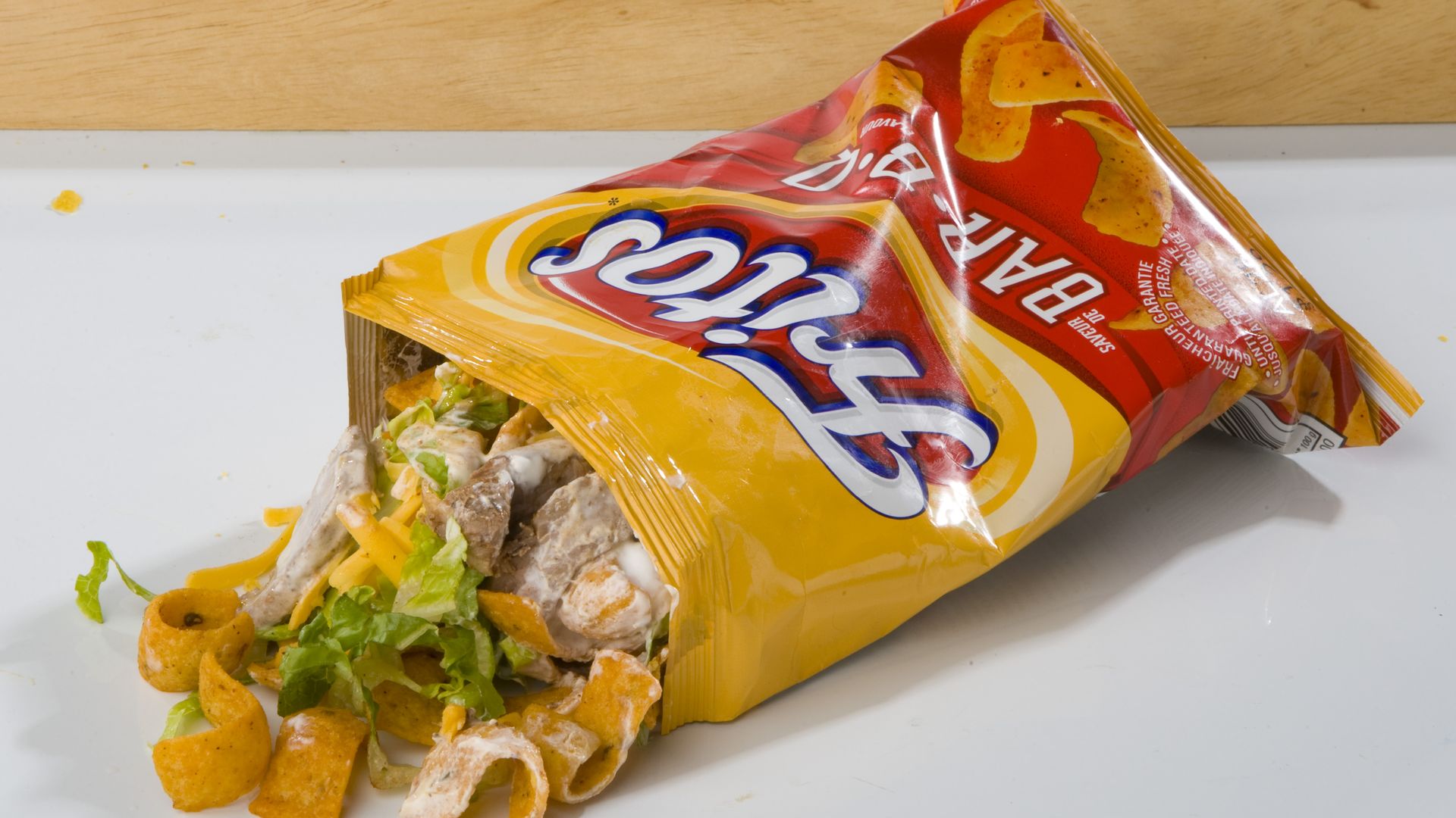A messy bag of fritos corn chips with grilled steak, cheese, salsa, sour cream and lettuce. 