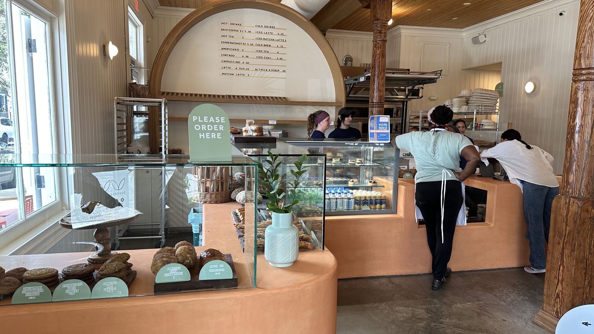 Employees chat near display cases inside a modern-designed bakery.