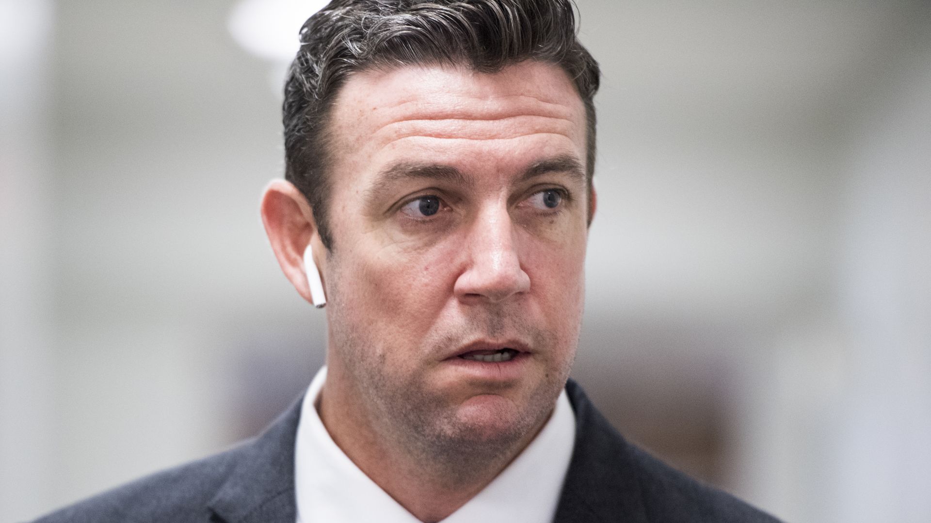 In this image, Duncan Hunter wears a suit and Airpods and walks down a hall.