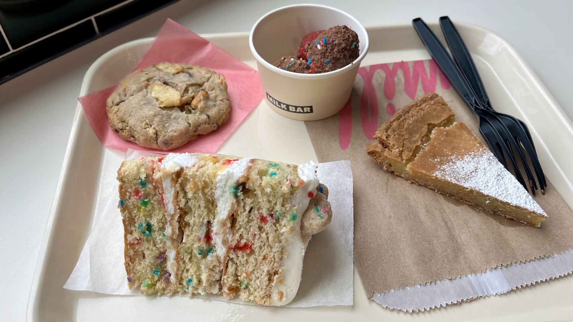 A tray with a multi-layered piece of cake, cookie, cup with cake balls and piece of pie with powdered sugar.