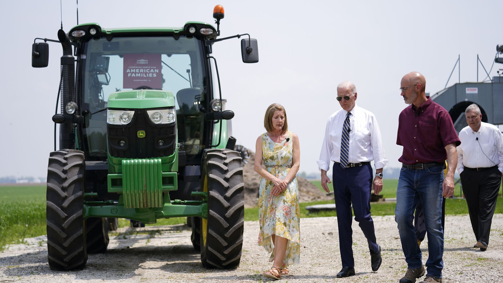 President Biden and Agriculture Secretary Tom Vilsack walking on a farm next to a tractor.