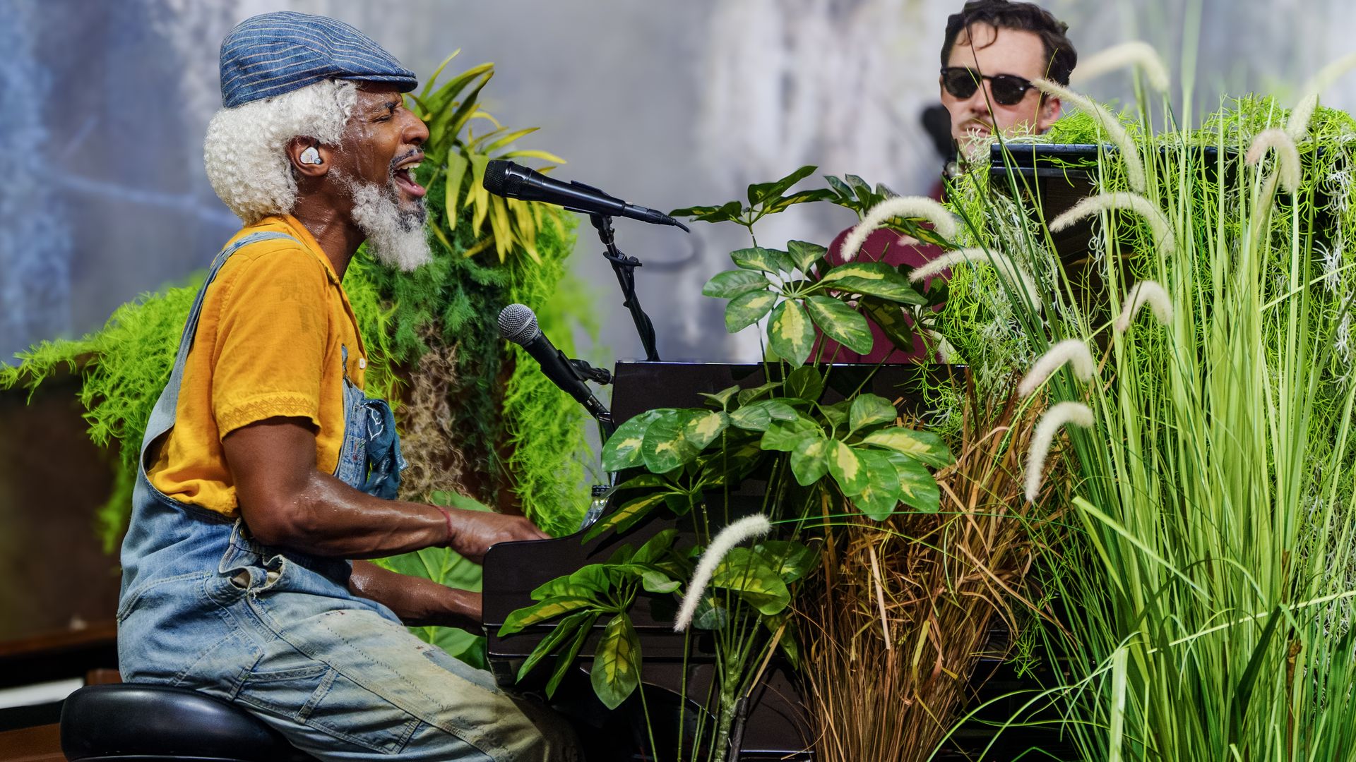 Image shows Jon Batiste in a wig and overalls while playing the piano.