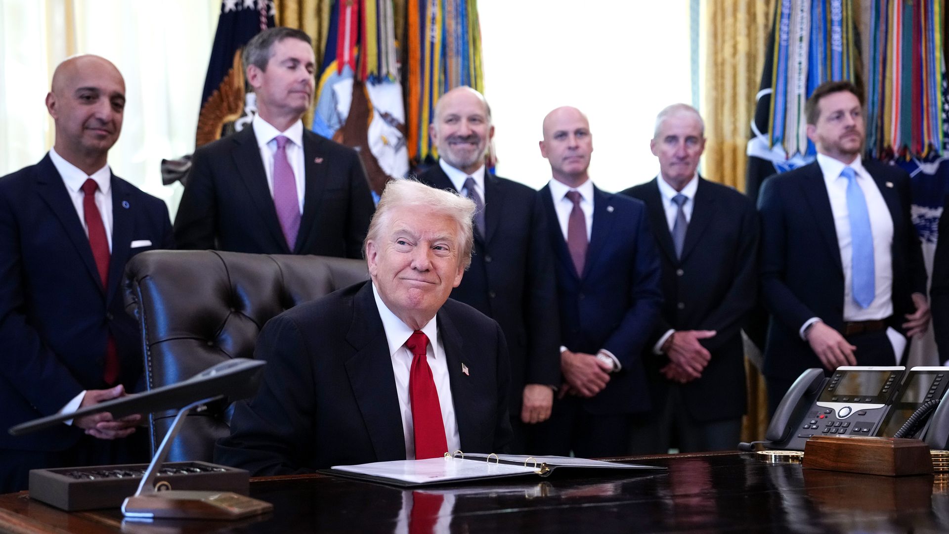 Trump wearing a navy suit, white shirt and red tie surrounded by other pharmaceutical industry members