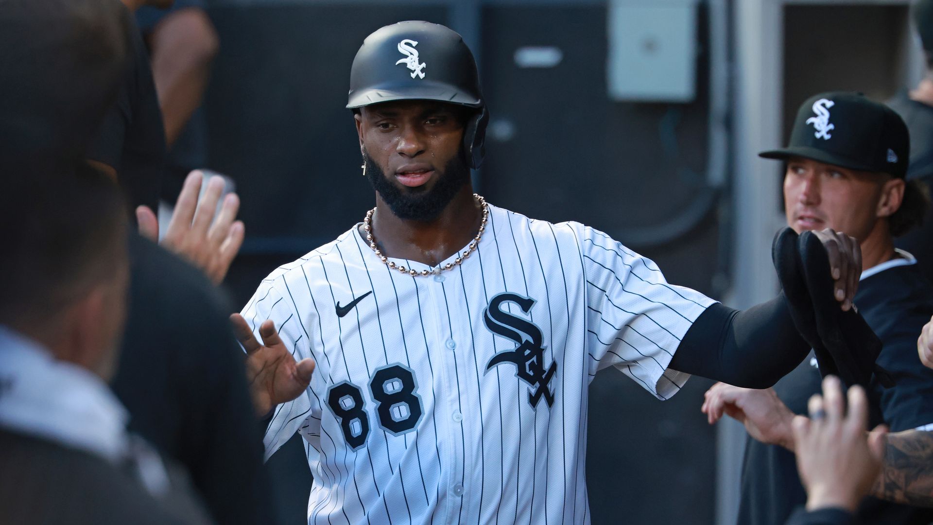 Chicago White Sox player wearing white pinstripe uniform with number 88 and black helmet, giving high-fives in dugout during game.