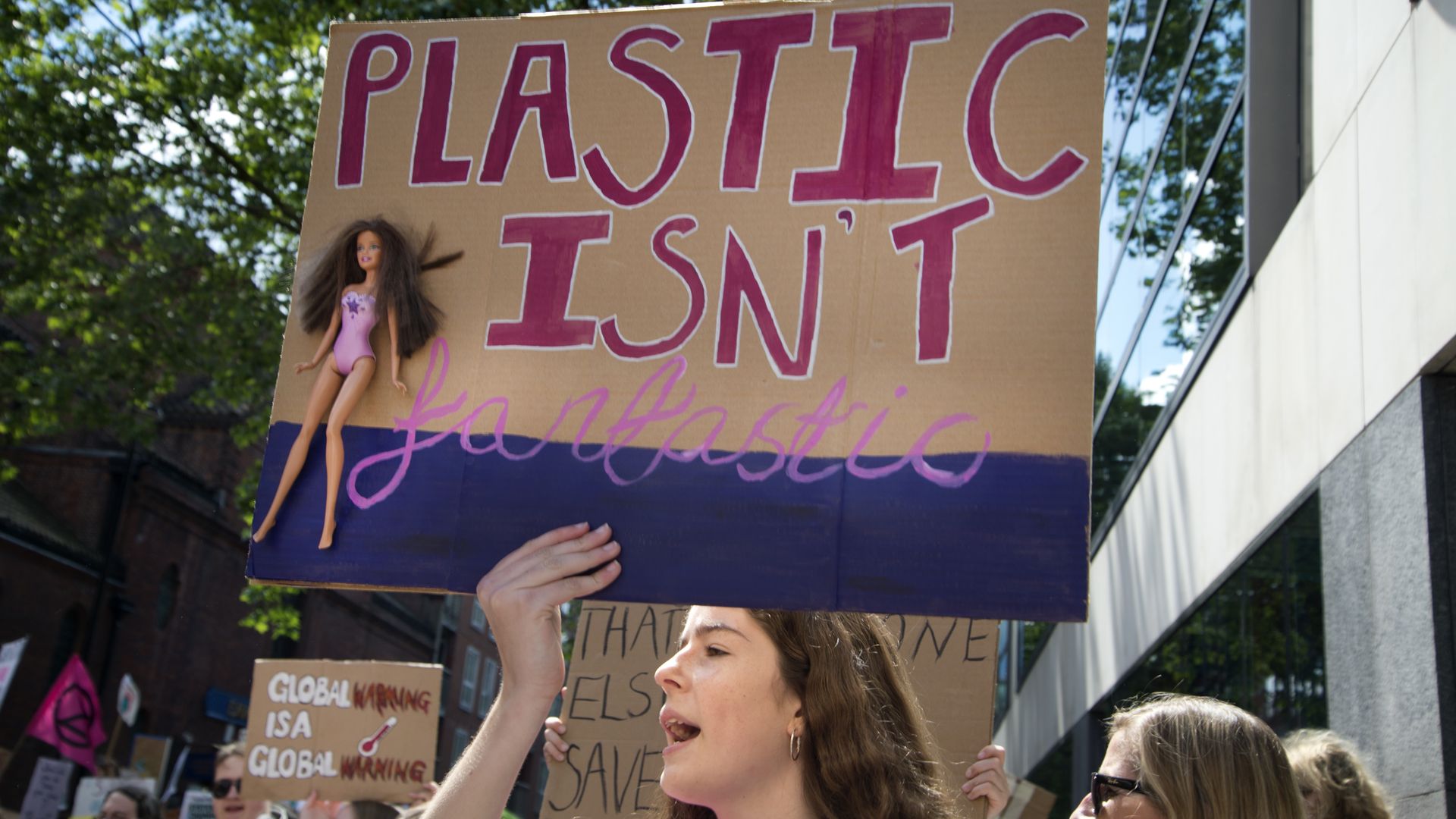 A girl holds a sign with a Barbie doll which says 'Plastic is not fantastic'. 