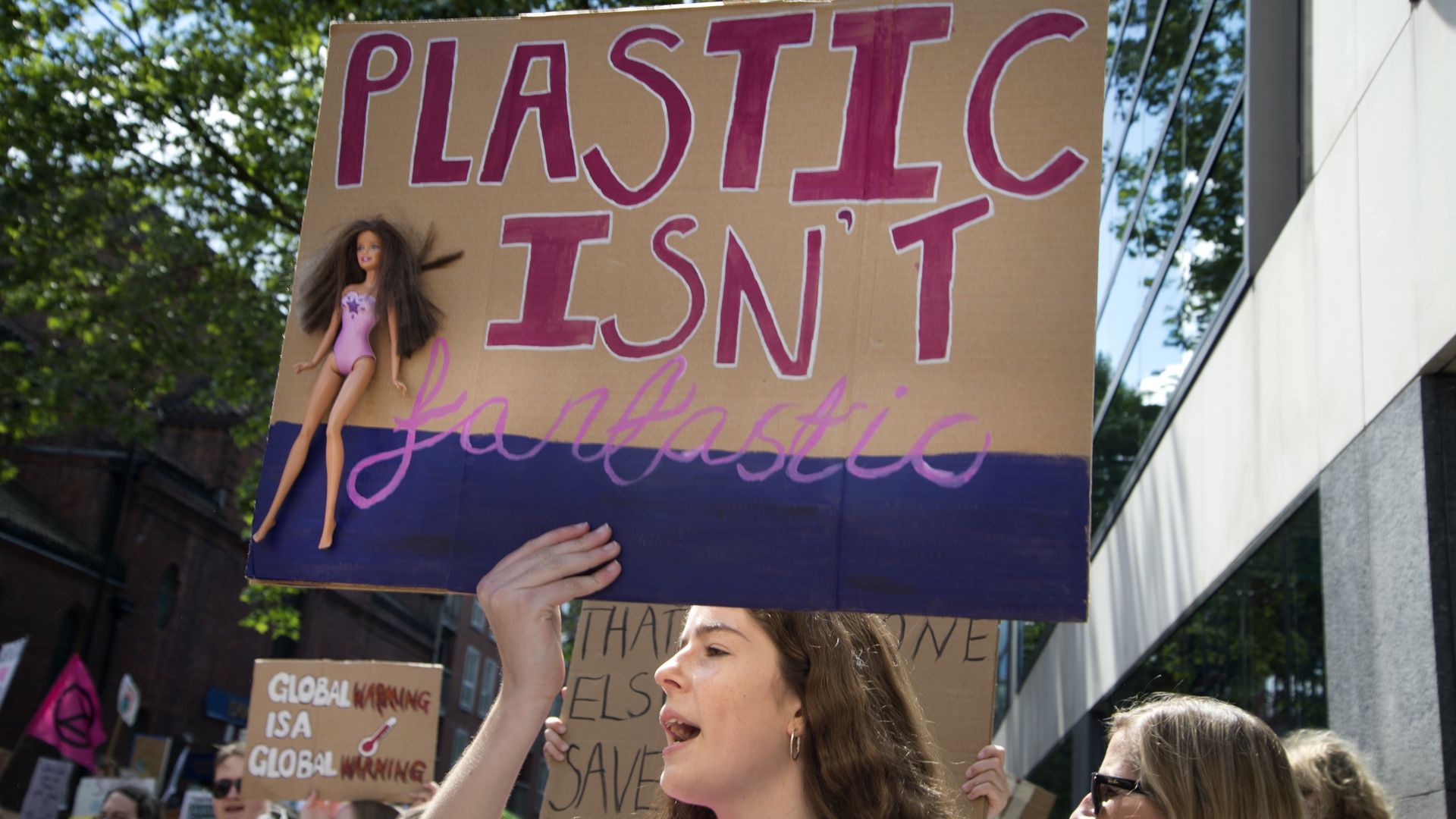 A girl holds a sign with a Barbie doll which says 'Plastic is not fantastic'.