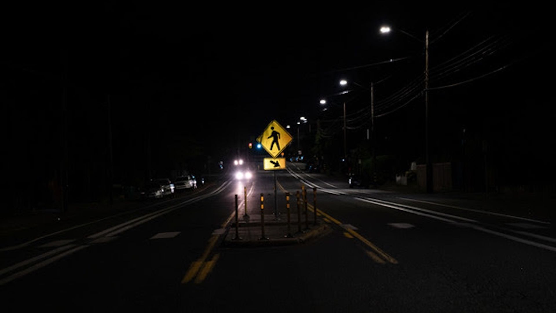 A photo of a dark, dimly lit road with a barely visible pedestrian walk sign.