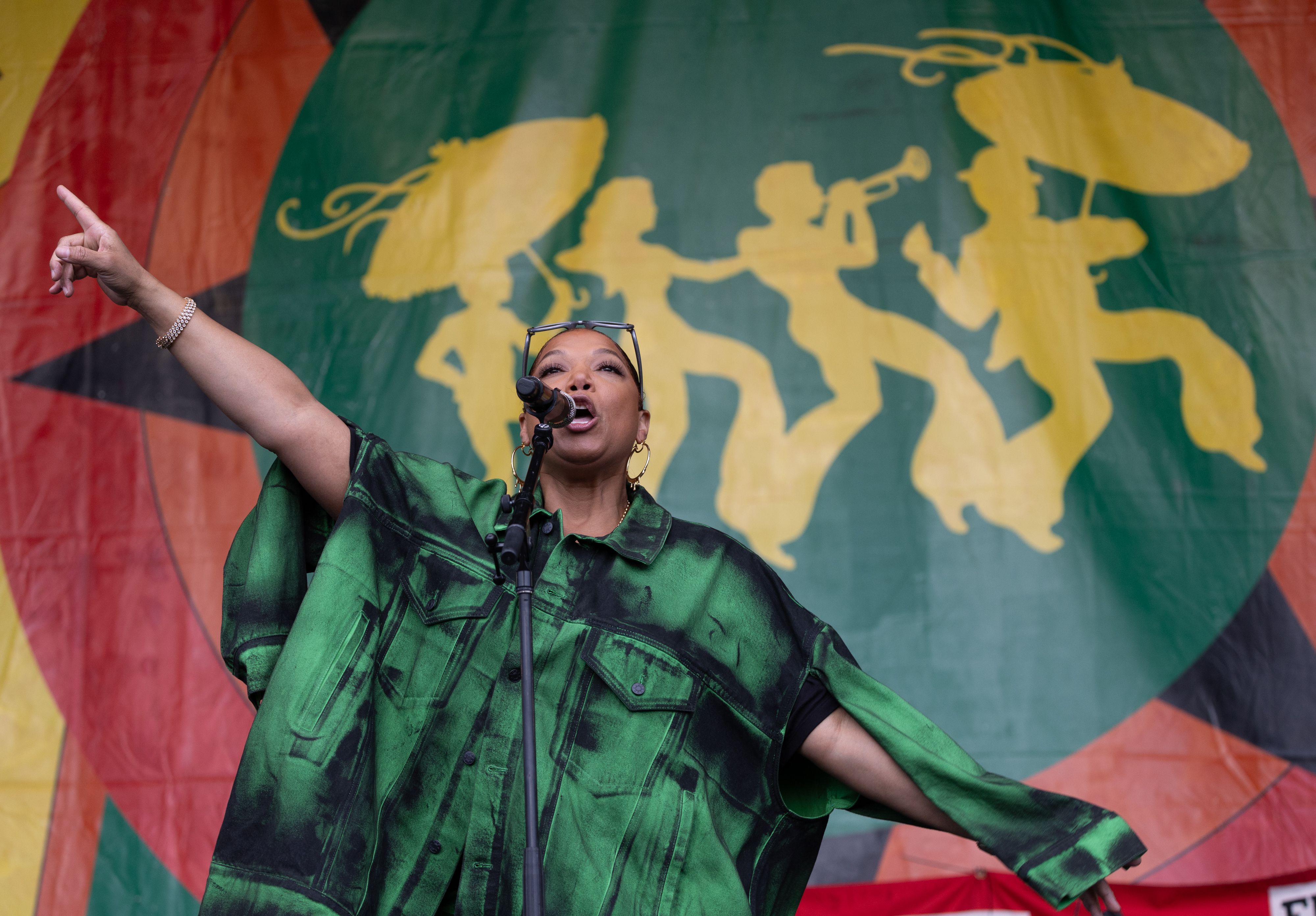 Queen Latifah sings into a microphone with both arms in the air, angled diagonally away from her body. 