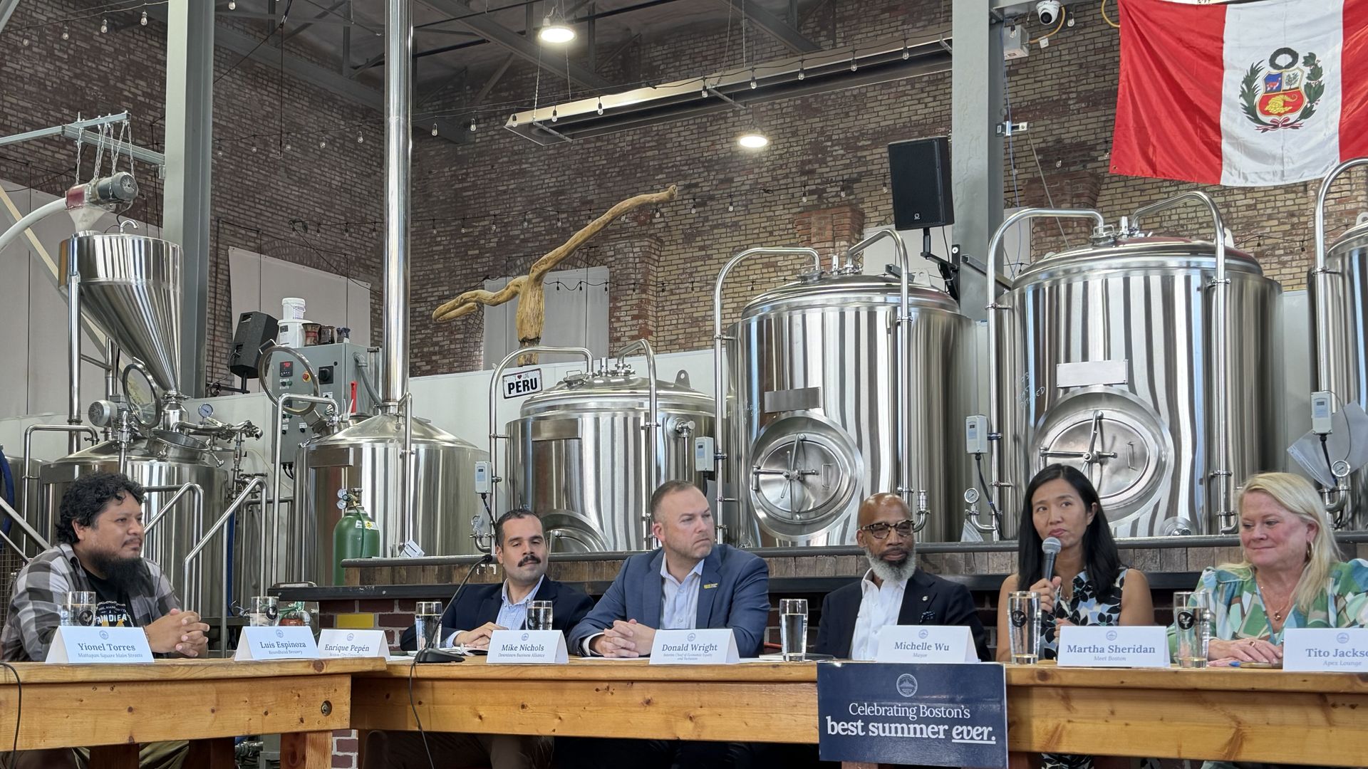 Boston officials and business leaders sit at a U-shaped wooden table for a business roundtable following a trio of summer events. Wu, right, is speaking and holding up the microphone as she speaks in Roundhead Brewing in Hyde Park. 