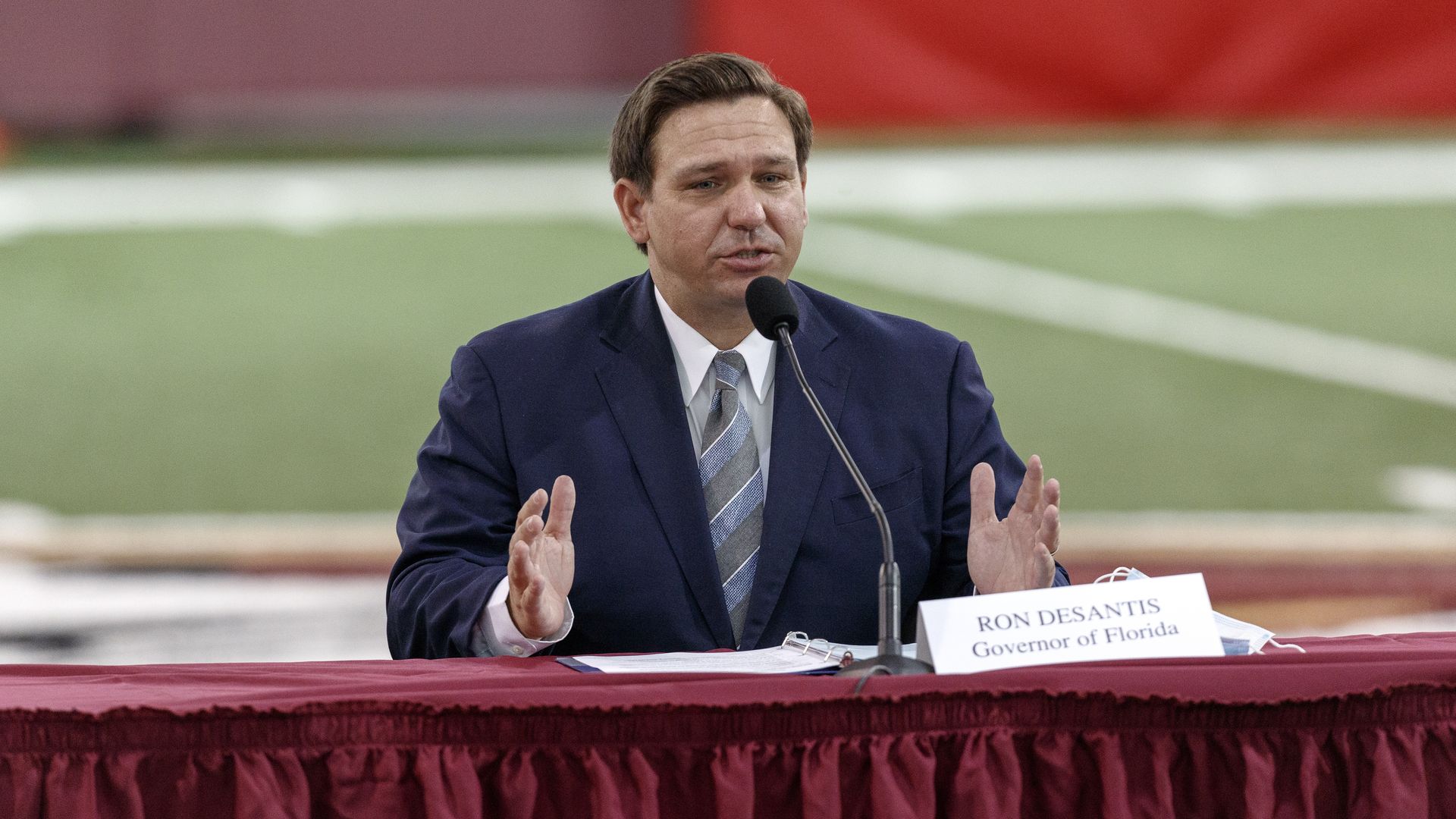 Ron DeSantis sits at a red cloth table with a name tag in front of him 