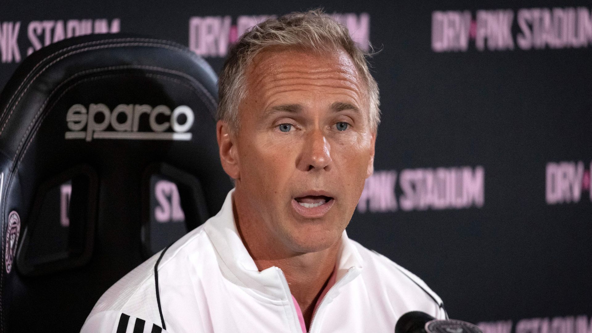 An individual wearing a white athletic workout suit sits in a high-back leather chair with "eparco" on the headrest