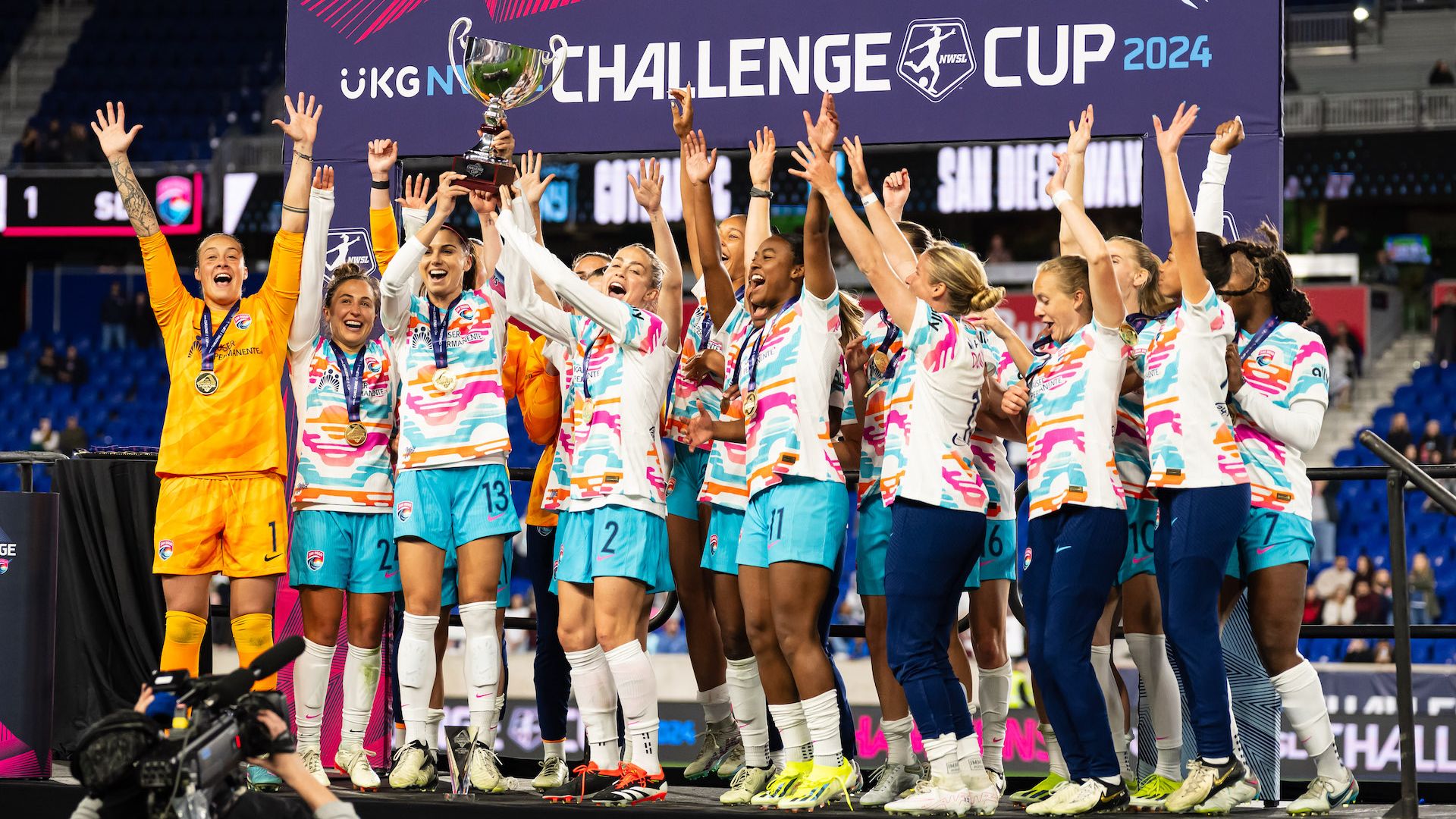 San Diego Wave soccer players lift a trophy on stage after winning the NWSL Challenge Cup. 