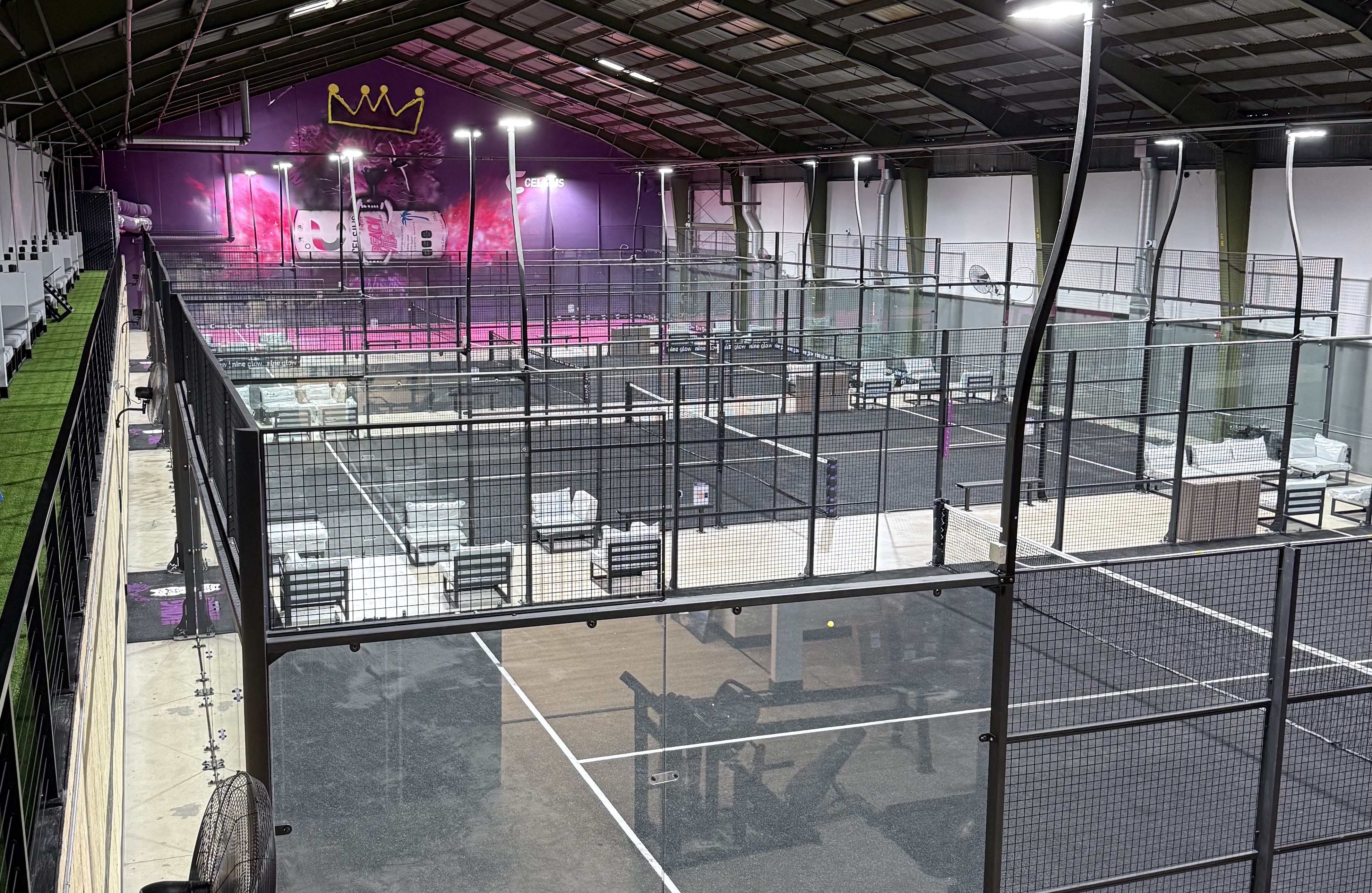 A warehouse with several padel courts and a pink and purple graffiti mural on a far wall. 
