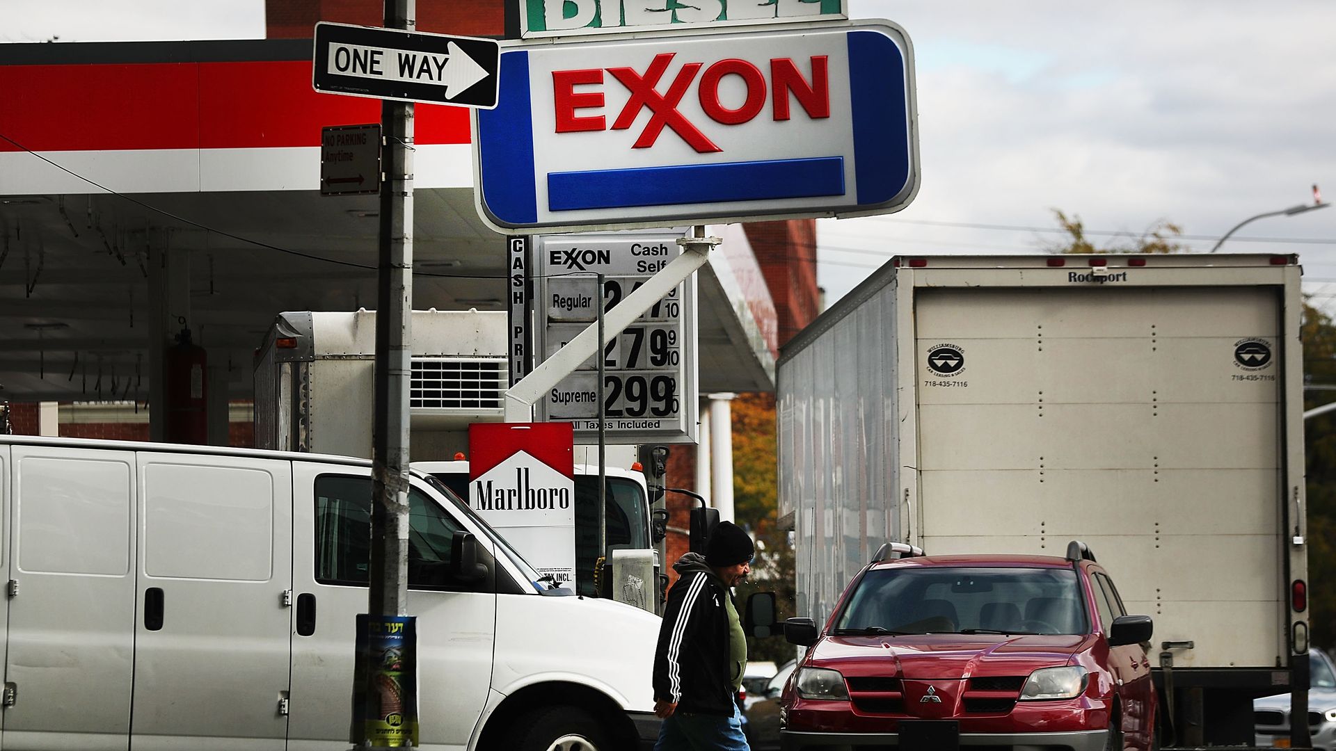 In this image, a man walks underneath an Exxon sign at a gas station.