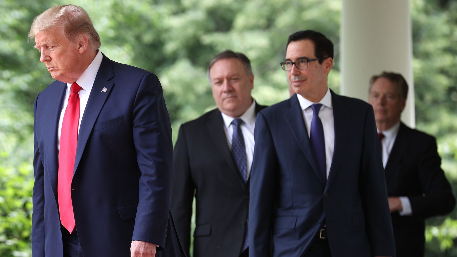 Mnuchin and Trump walk together in the foreground with Bill Barr in the background, all wearing suits and ties