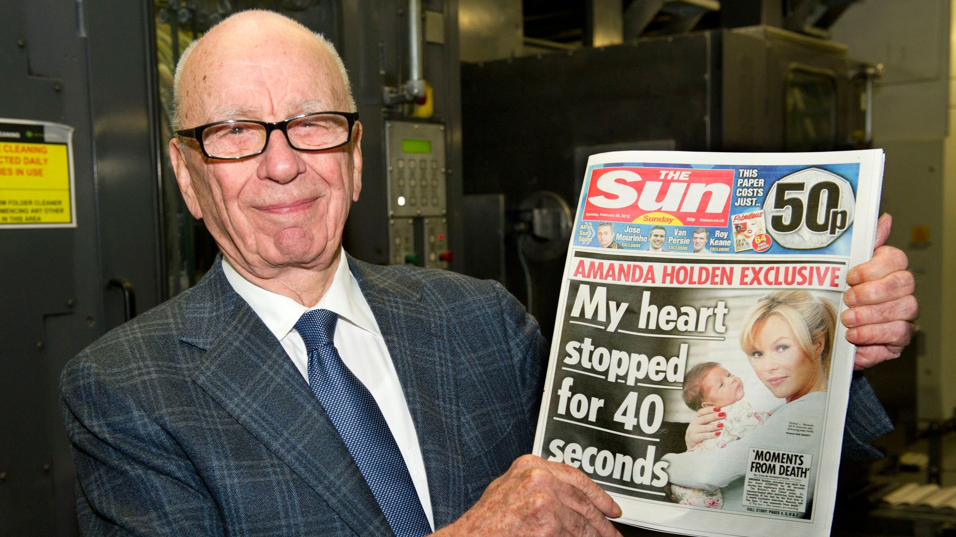 A photo of Rupert Murdoch smiling and holding a newspaper
