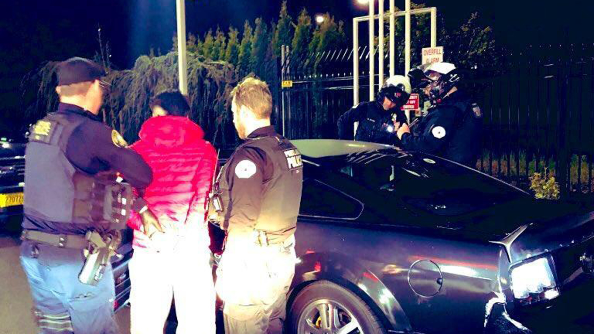 Two police arrest a driver in red in front of his car for illegal street racing