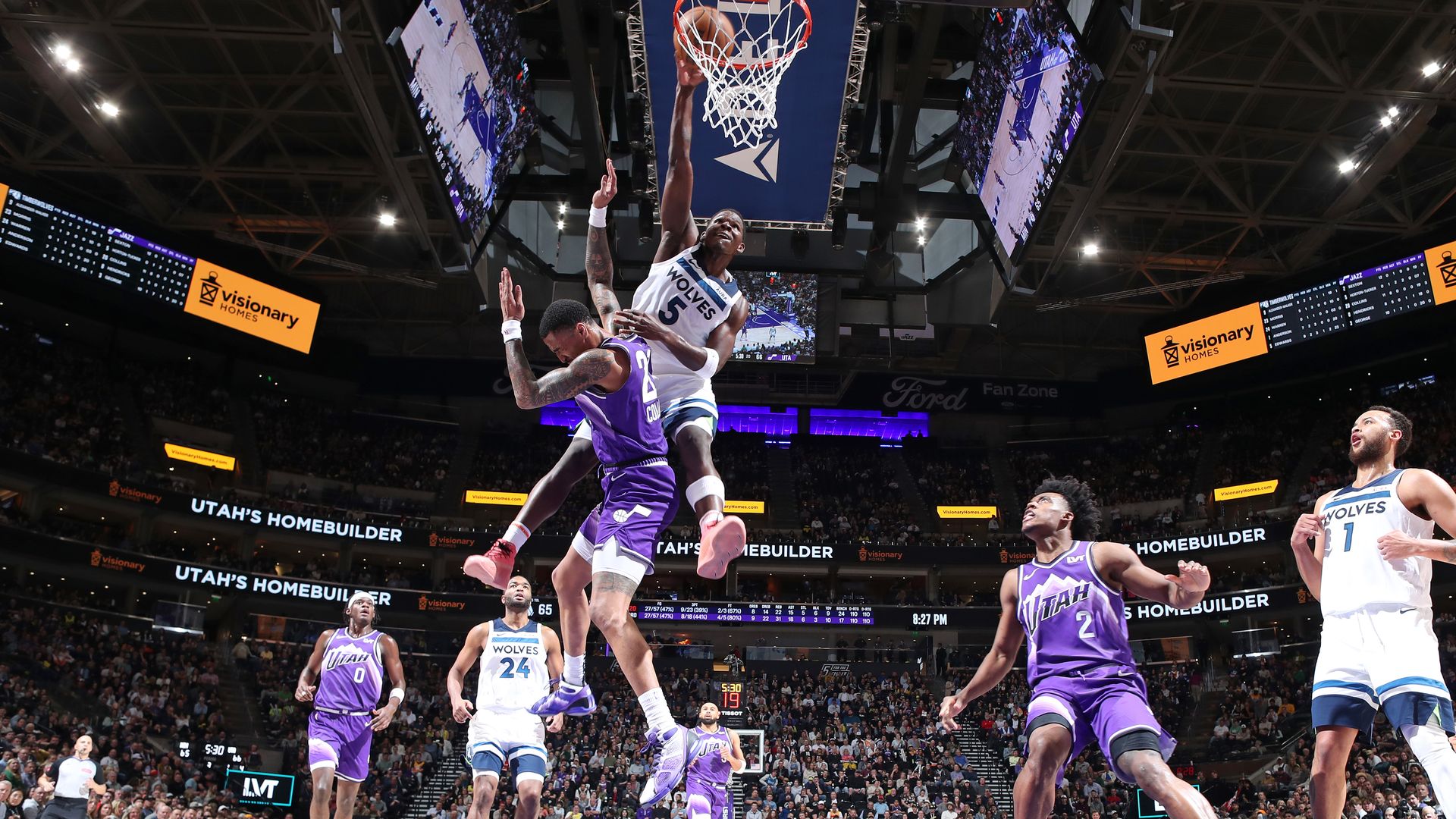 A basketball player dunks a ball while others run to the basket.
