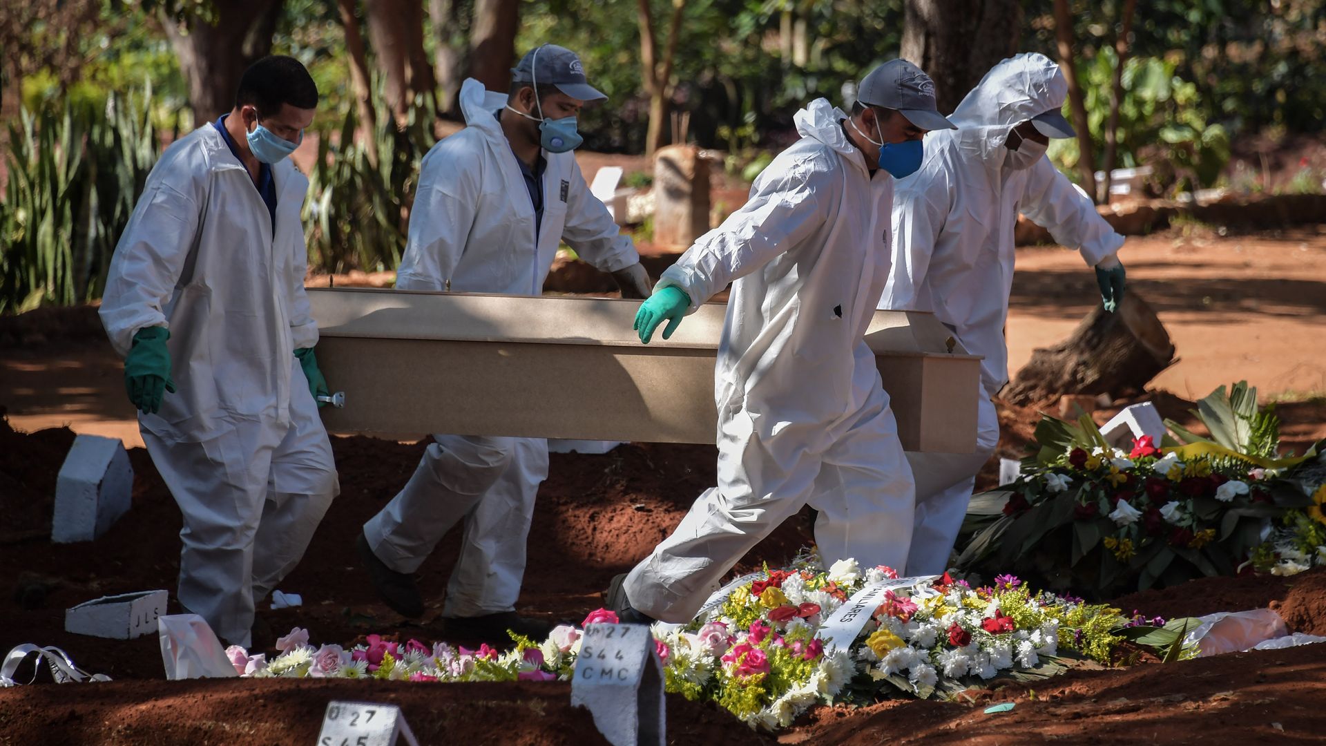 In this image, four men in hazmat suits carry a coffin