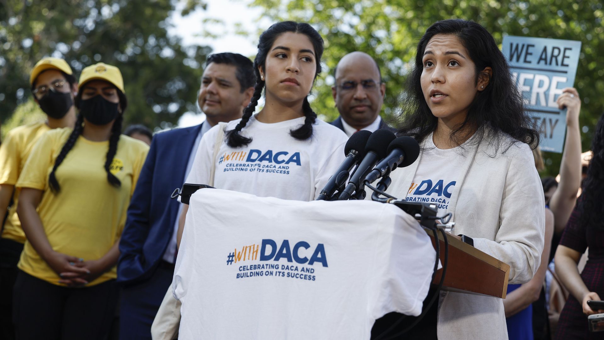 Photo of two activists speaking while holding a T-shirt that says "#WithDACA"