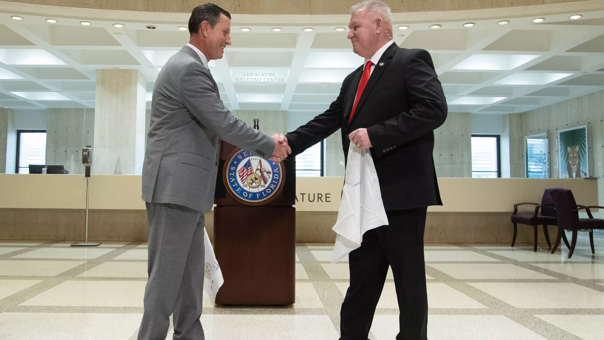 Two men in suits shake hands while holding white handkerchiefs 