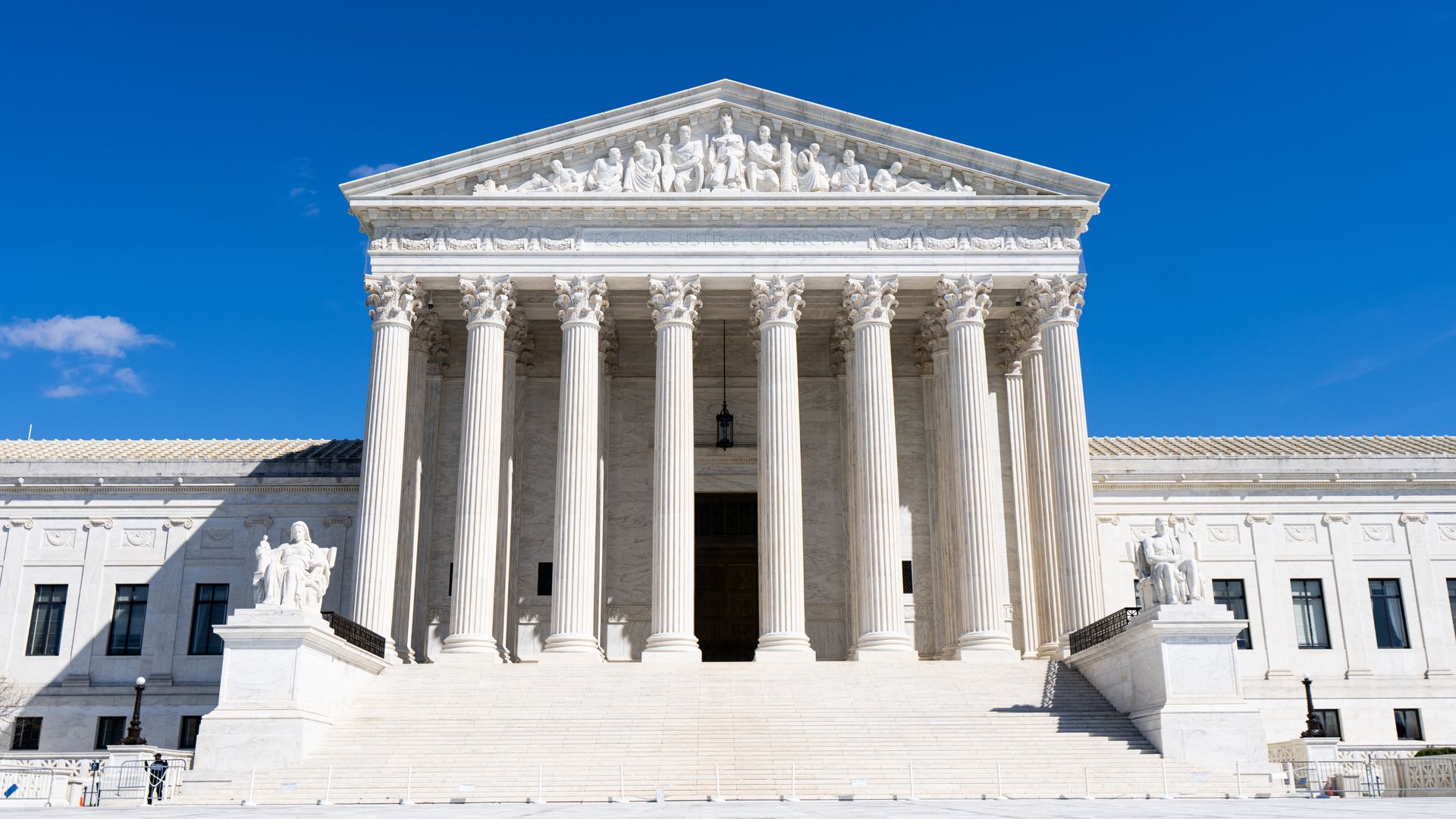 The facade of the U.S. Supreme Court building is lit in bright sun with a blue sky behind.
