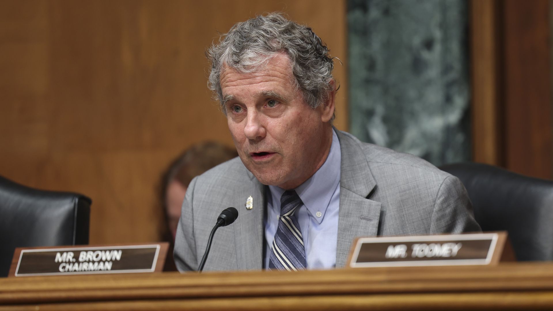 Sen. Sherrod Brown in a gray suit, seated behind his nameplate during Senate testimony