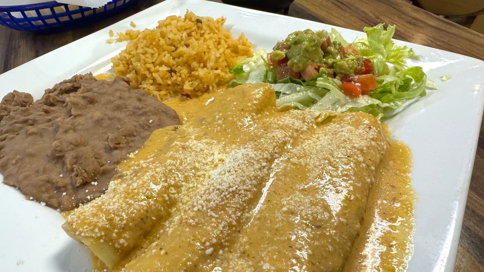 A plate of chicken enchiladas with bean, rice and a salad. 