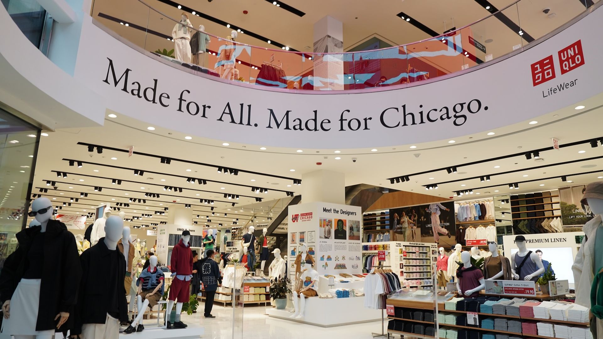 Bright Uniqlo store interior with a curved banner reading "Made for All. Made for Chicago." Ground-floor mannequins in white and neutral outfits; glass balcony and neat clothing displays fill the space.
