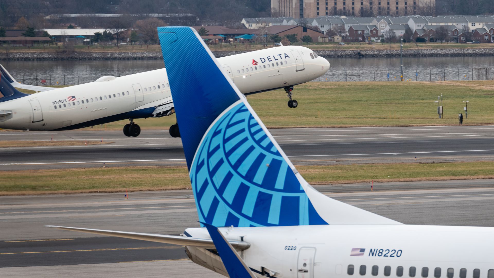 Photo of a Delta airplane about to lift off in the background as a United airplane's tail is seen in the foreground of an airport