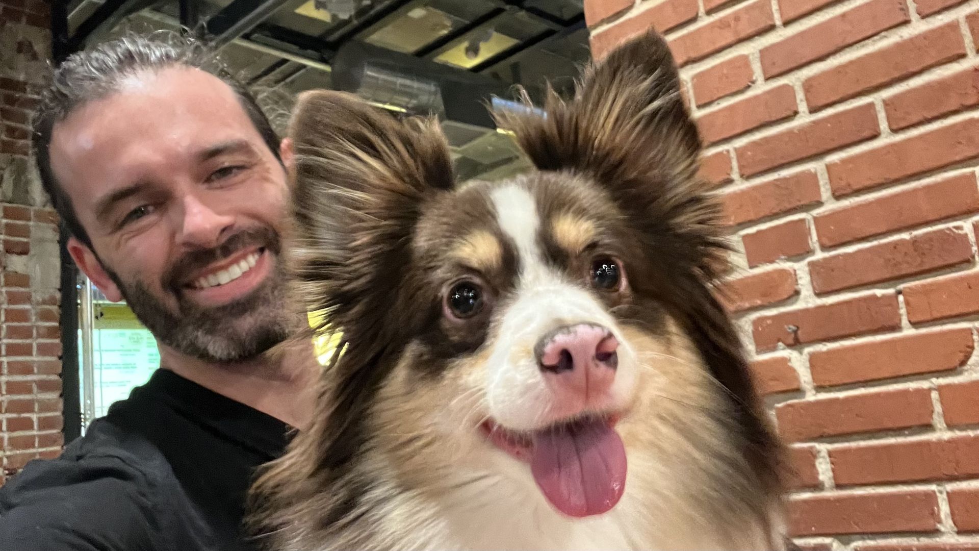 Photo of reporter Travis Meier and his dog Ollie next to a brick wall and an open garage door at River Bluff Brewing.