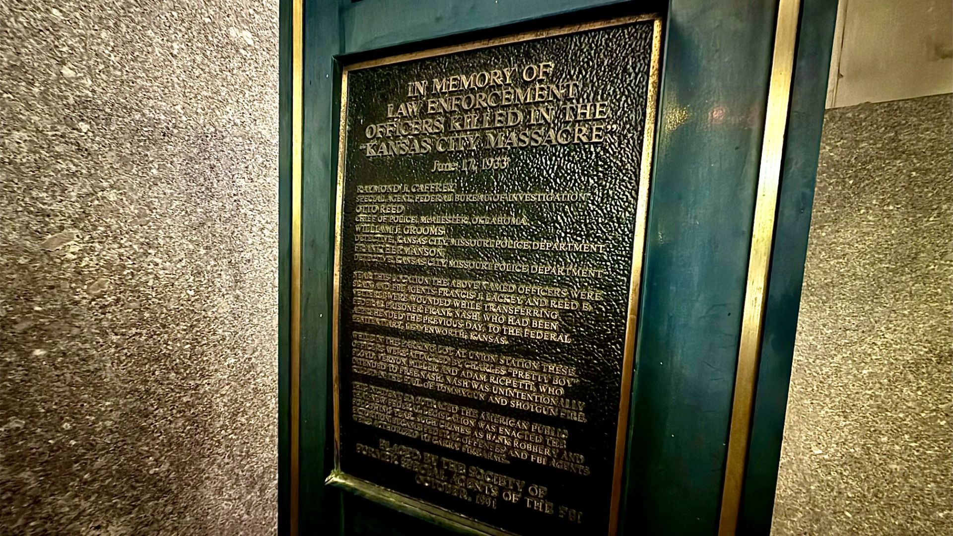 Bronze memorial plaque with gold text inside a green and gold frame, honoring law enforcement officers killed in the June 17, 1933 "Kansas City Massacre." Mounted on a textured wall.