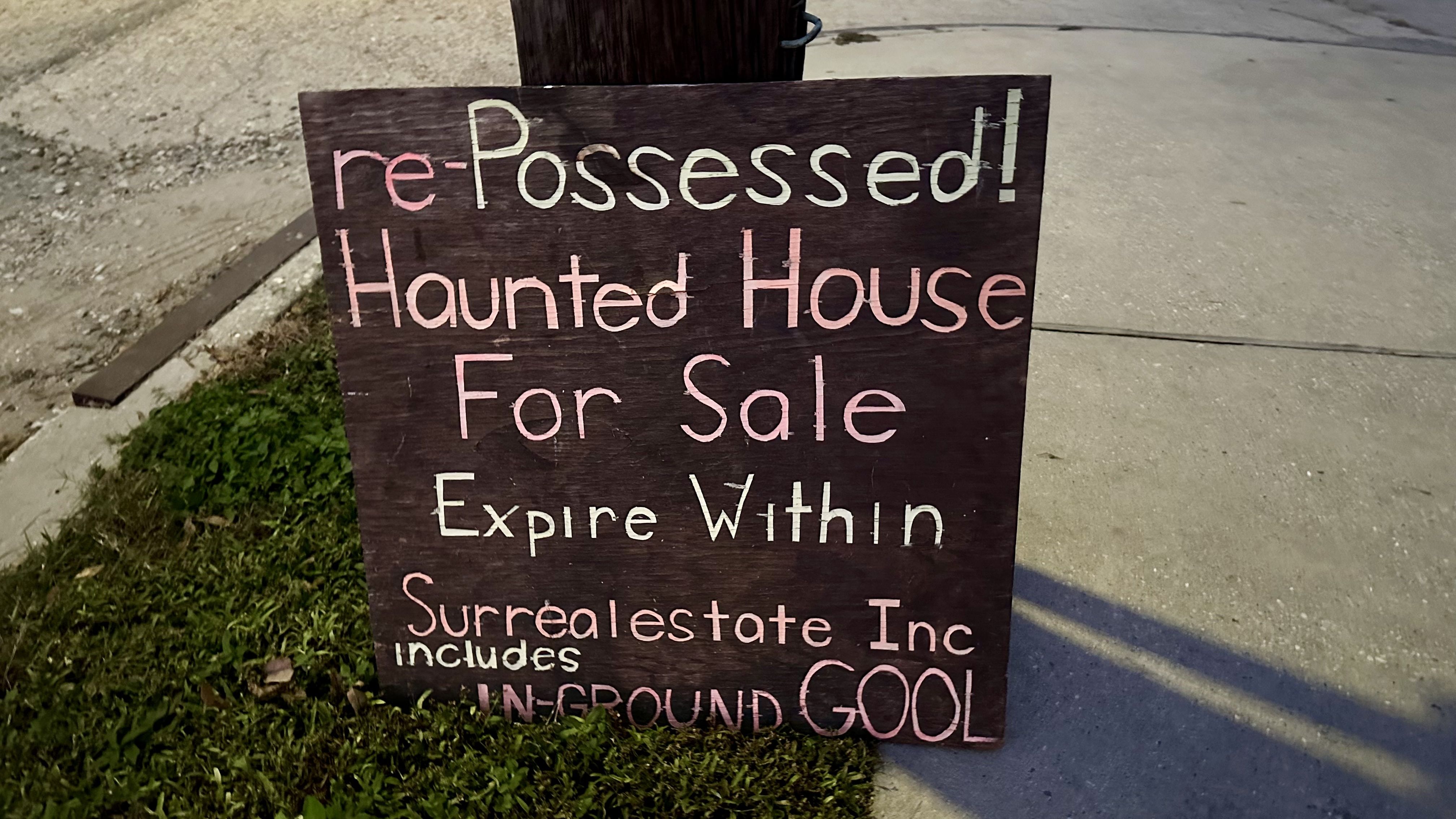 Image shows a sign that says "Re-Possessed! Haunted House for sale. Expire within. Surrealestate Inc. includes in-ground GOOL."