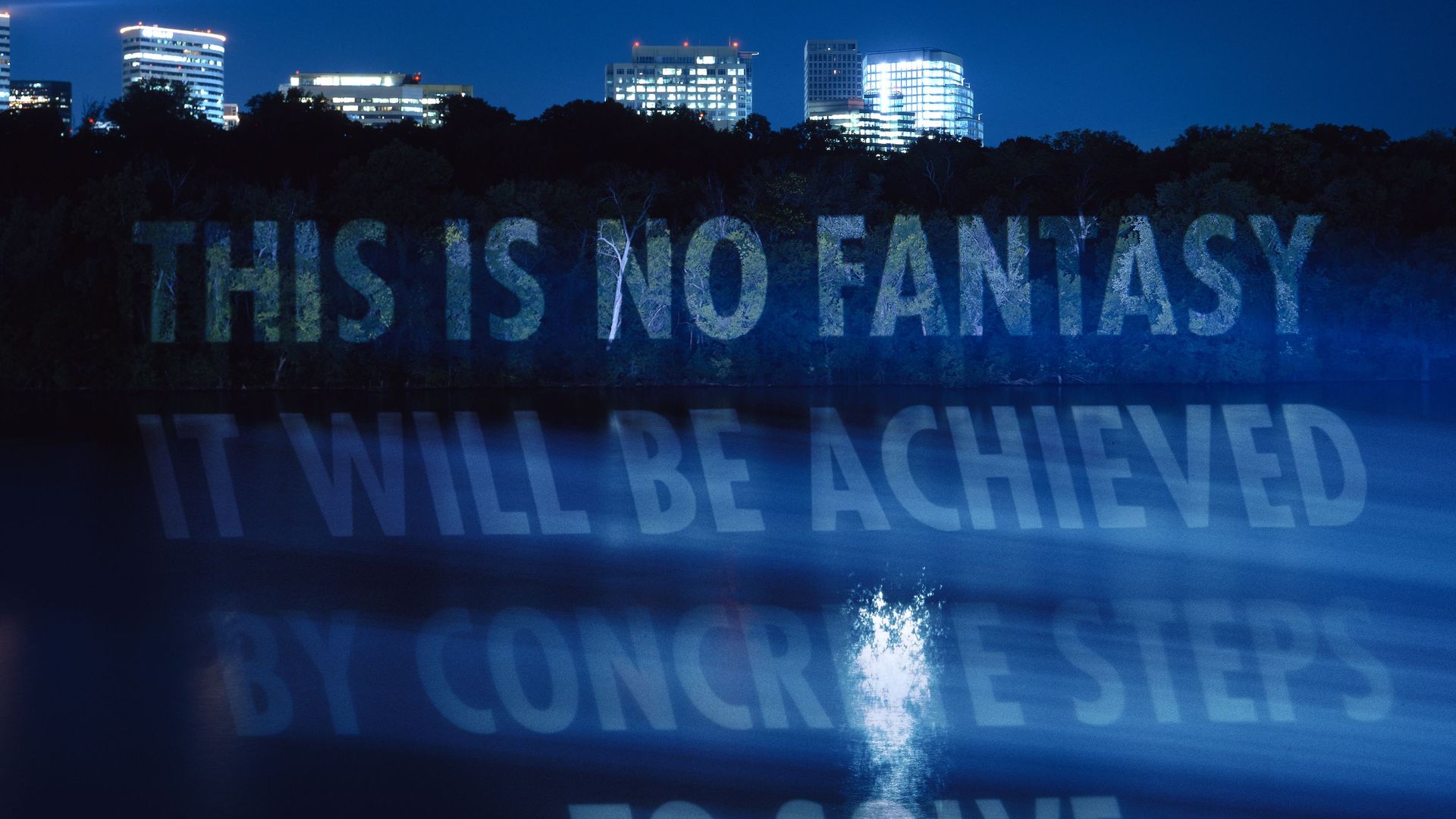 A light projection at night on the trees that line the banks of the Potomac River, that says "This is no fantasy It will be achieved by concrete steps."
