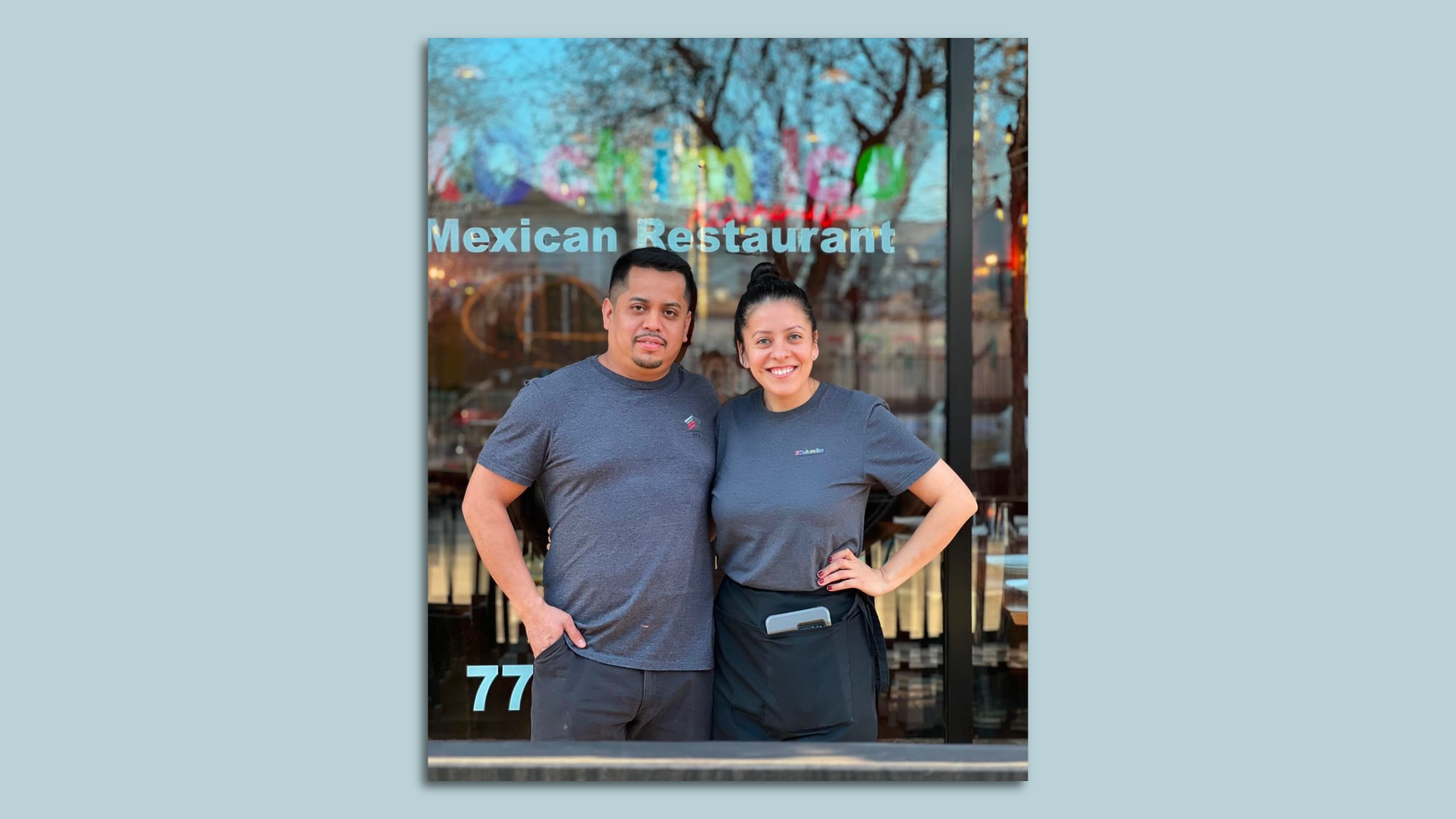Couple in blue shirts post in front of XOchimilco Mexican Restaurant sign.