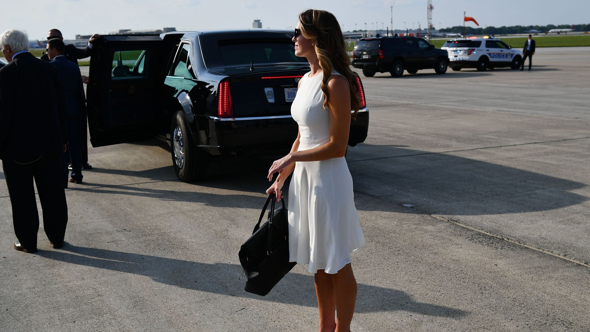 Hope Hicks stands outside wearing a white dress, heels and sunglasses