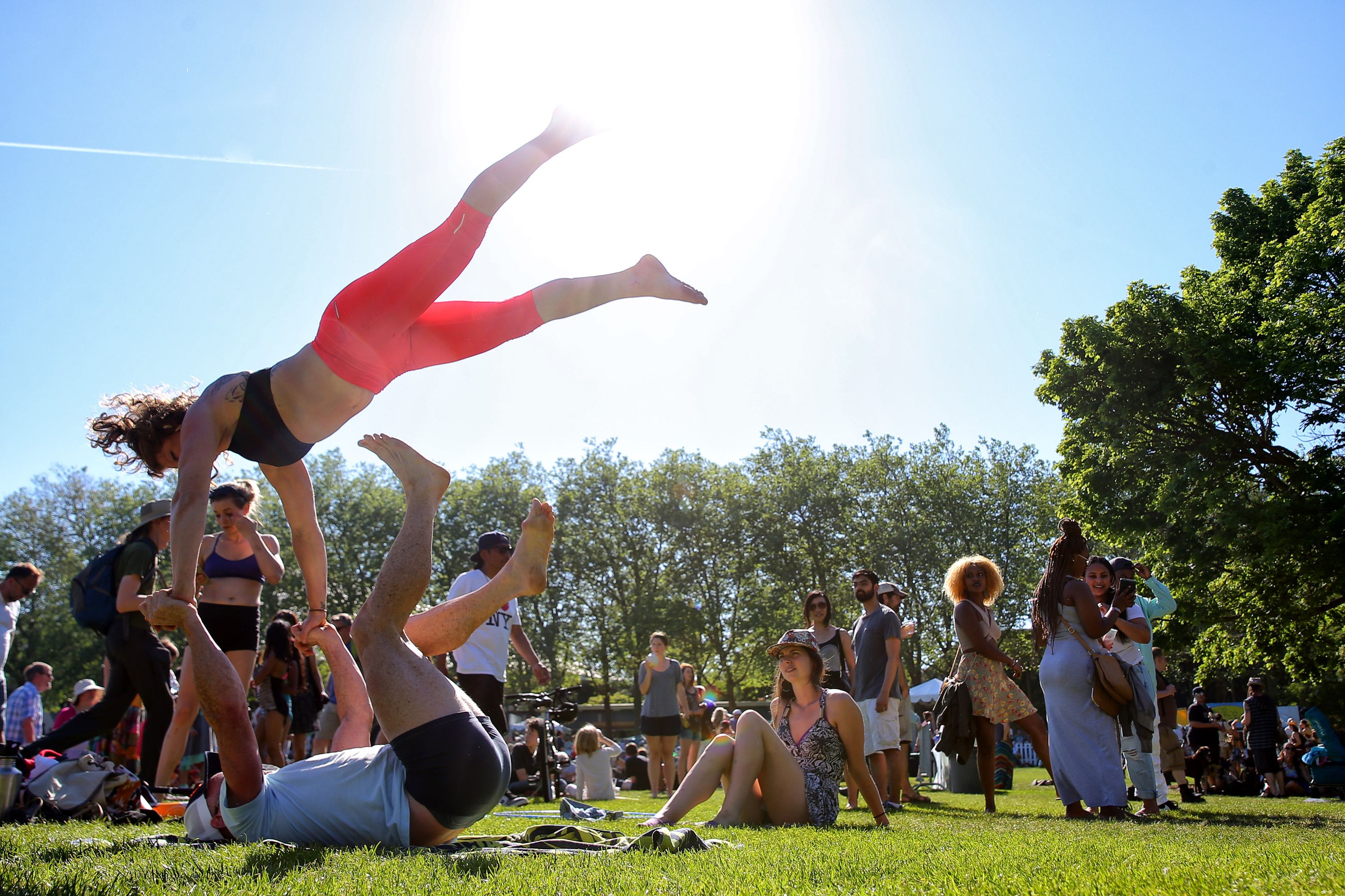 A woman is balanced in the air on the feet of a person laying in the grass.