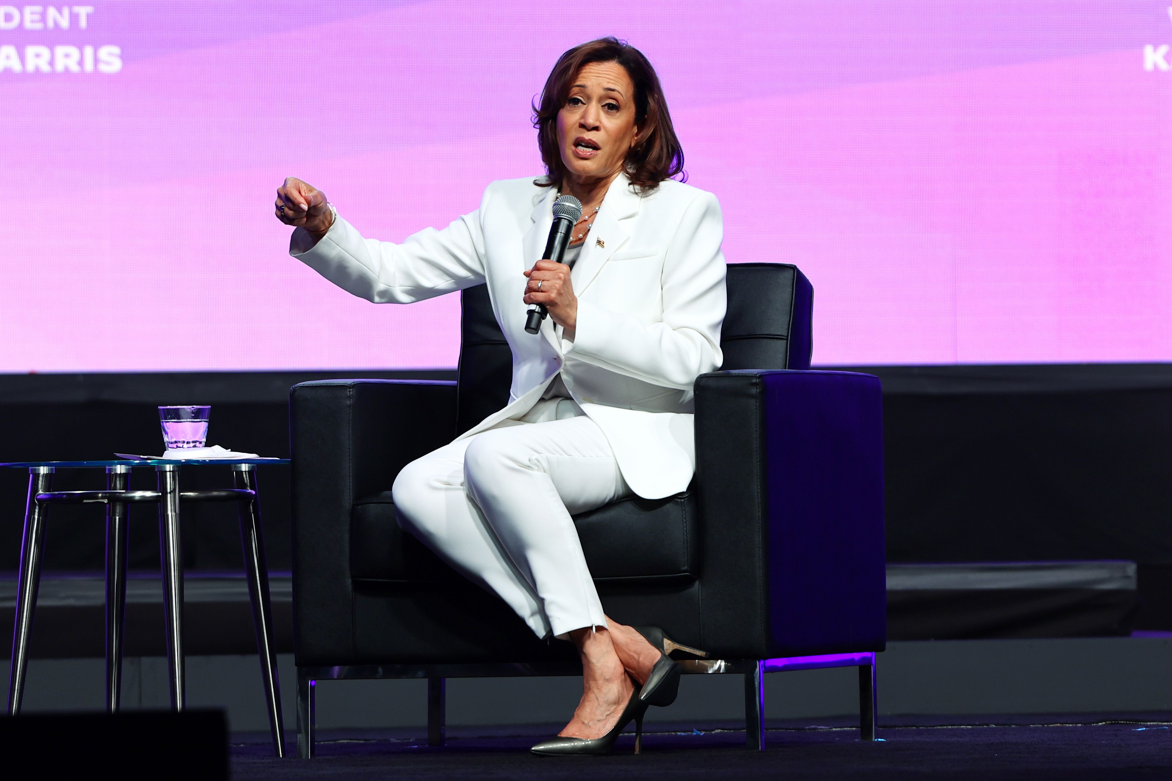 Photo shows Kamala Harris, wearing a white suit, talking on stage at Essence.