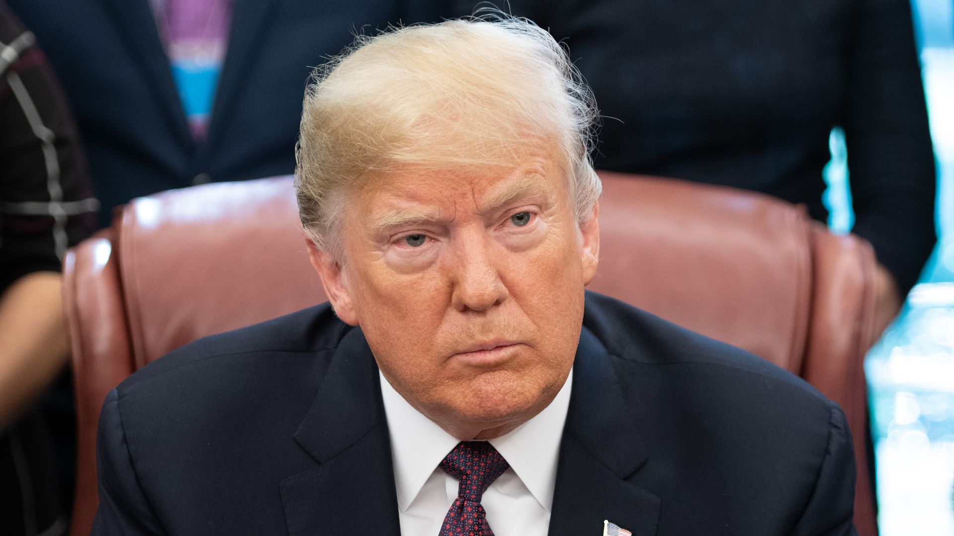 President Trump sits at his desk with his hands clasped together in front of him.