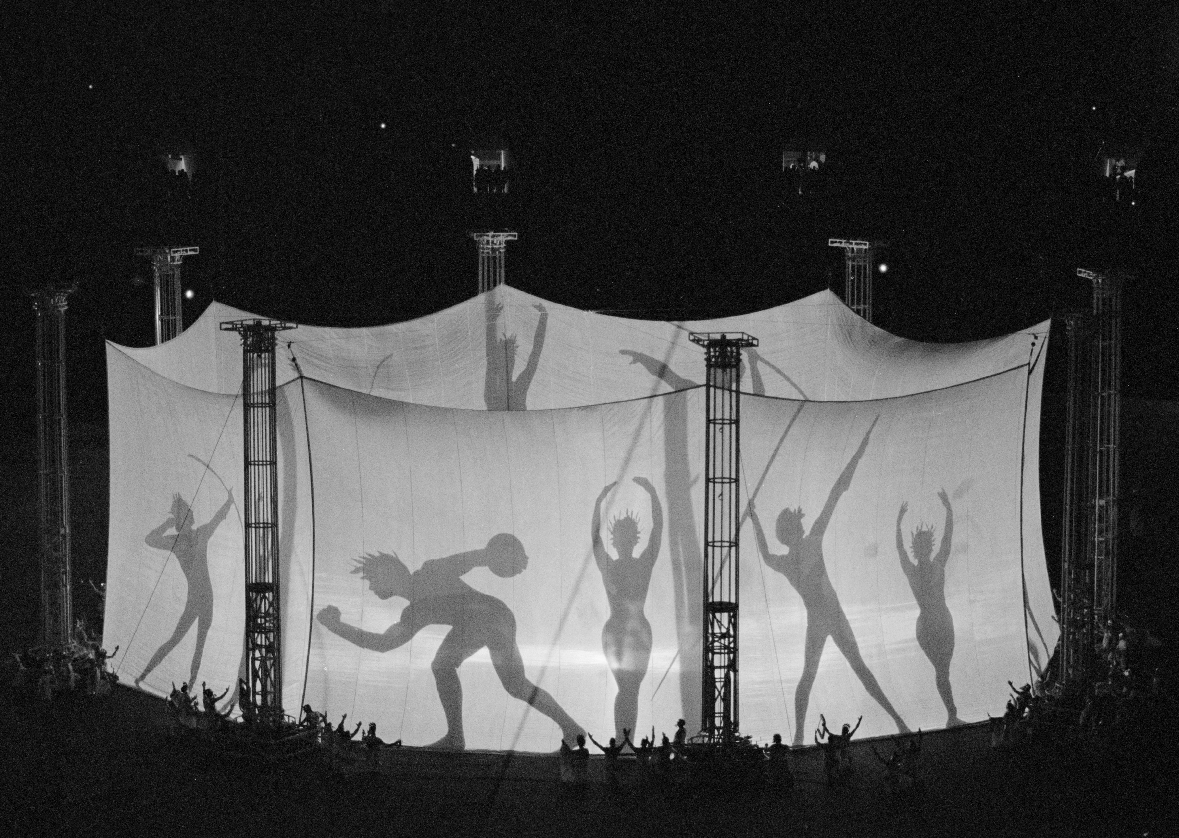 Backlit dancers perform in front of large screens, creating shadow silhouettes and giving them an oversized appearance