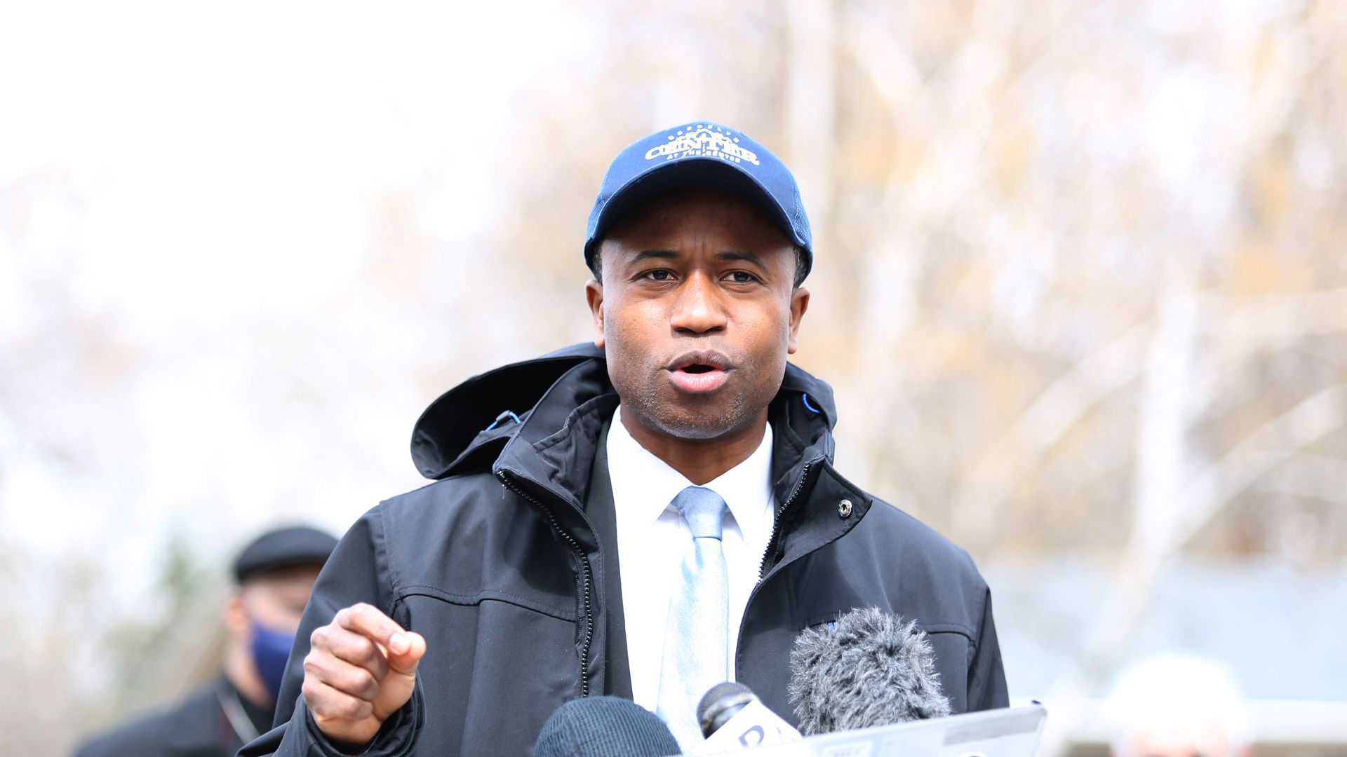 Brooklyn Center Mike Elliott gives a speech wearing a baseball cap and jacket 