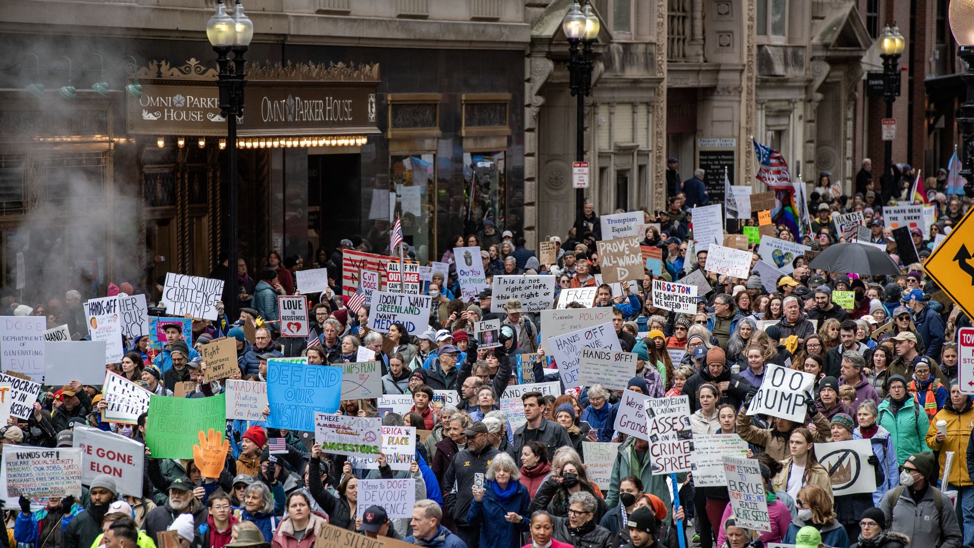 Swarms of people march and hold signs outside Omni Parker House, as they march from Boston Common to City Hall for the anti-Trump "Hands Off" protest.