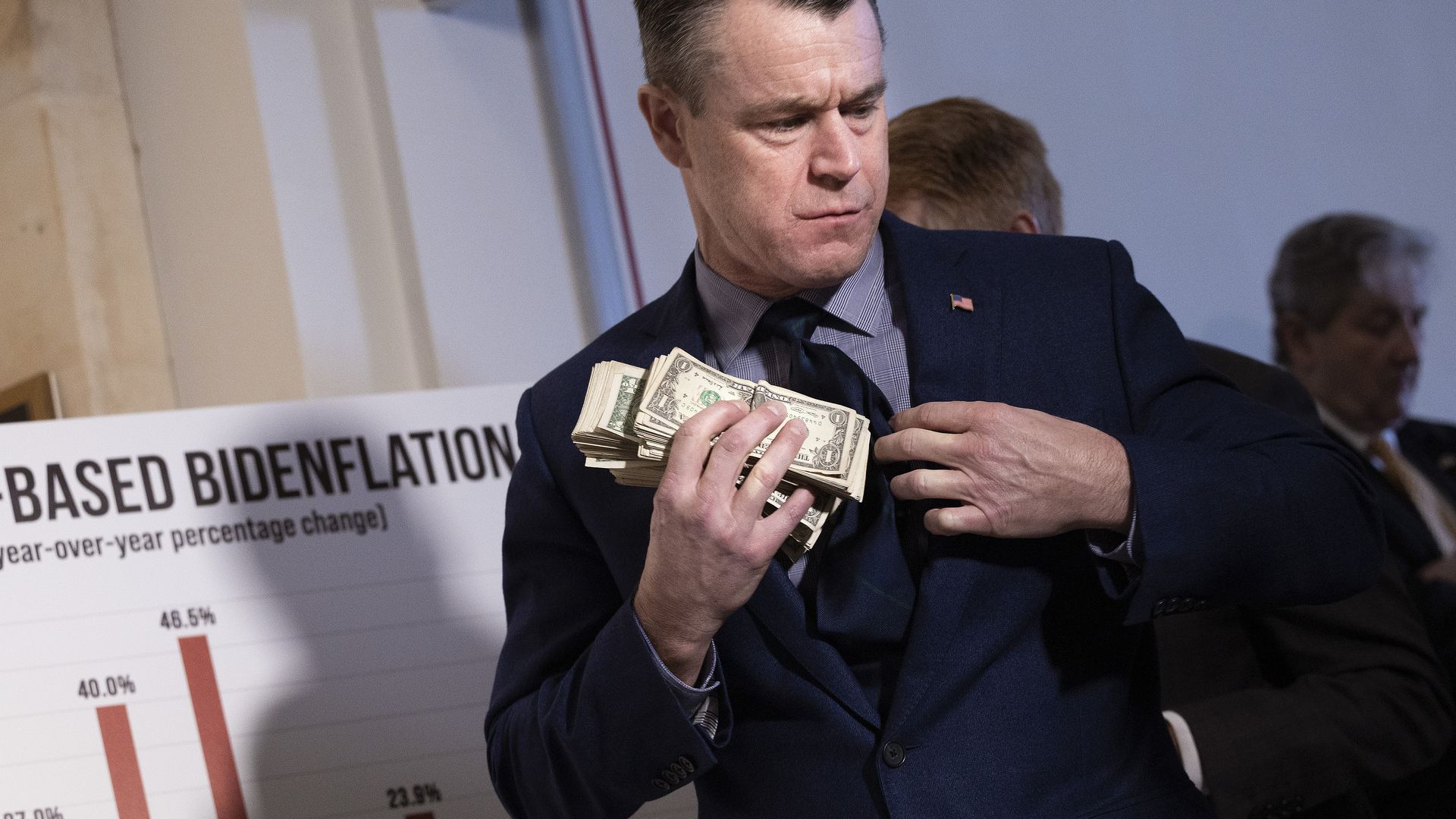 A senator is seen stuffing cash in his suit coat during a press conference to protest inflation.