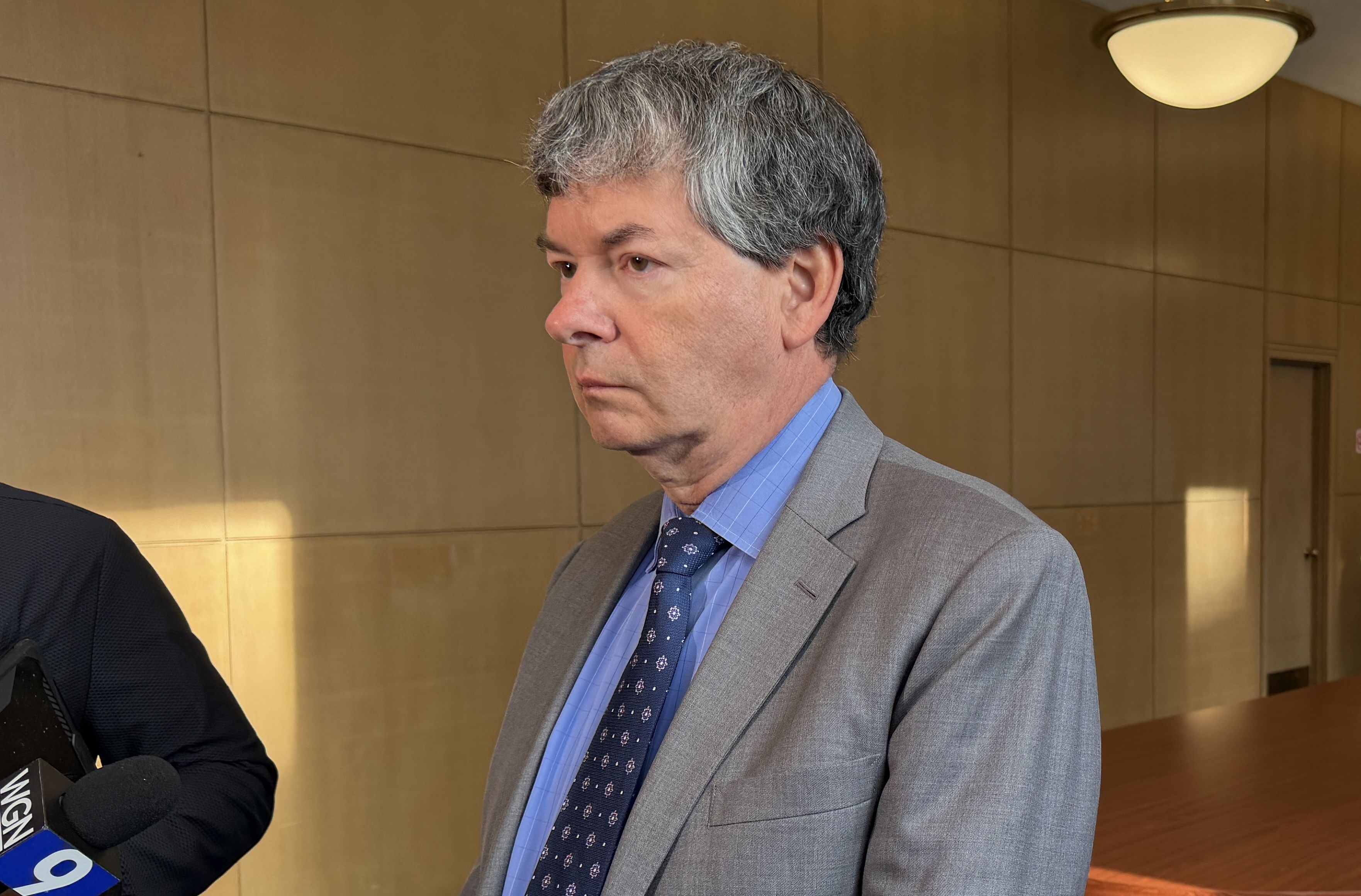 Man in a grey suit stands in a room. 